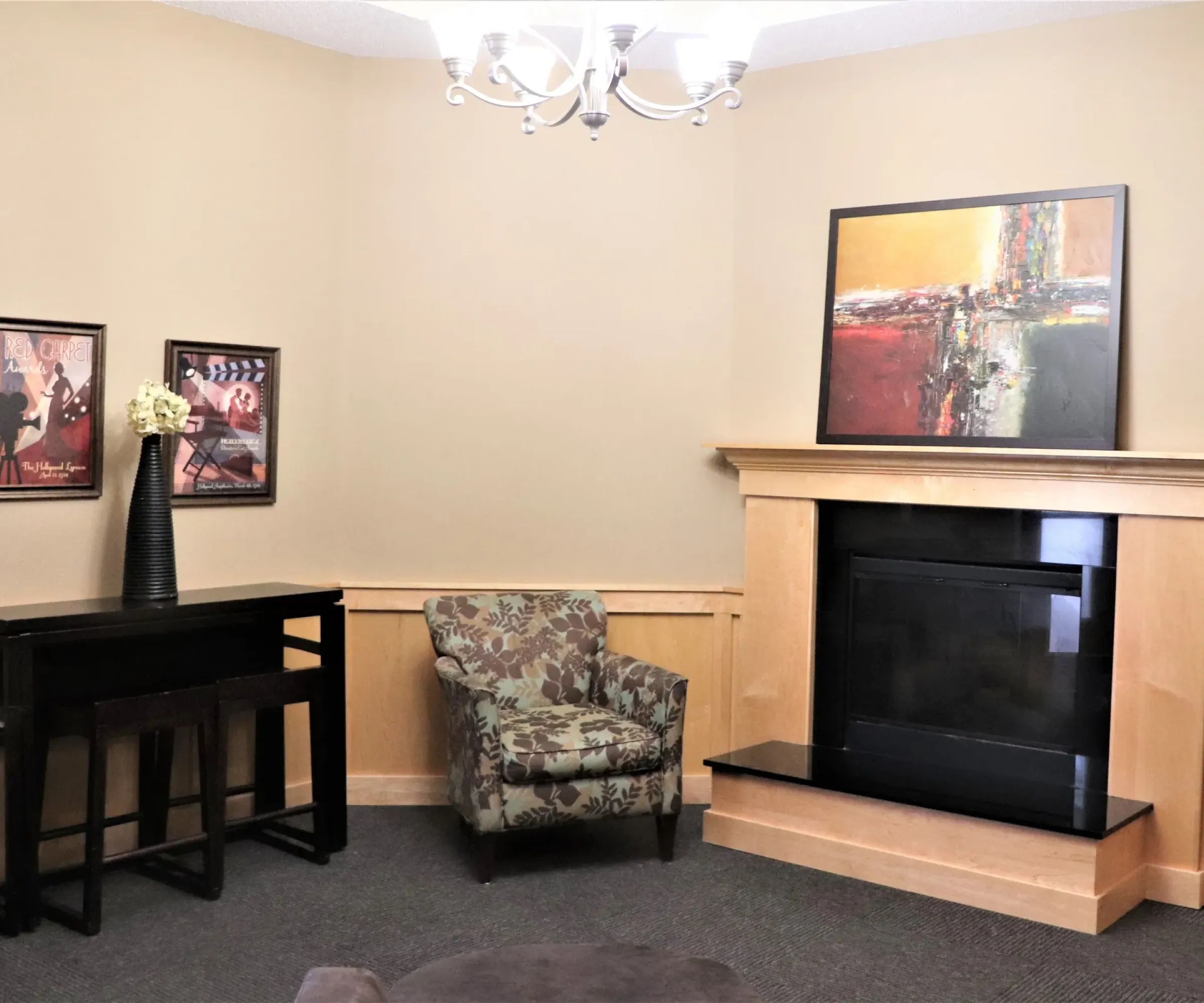 Aeon Affordable Homes and Community Cozy and affordable apartment home featuring floral armchairs, a small black table, art-adorned walls, and a wooden fireplace under a chandelier.