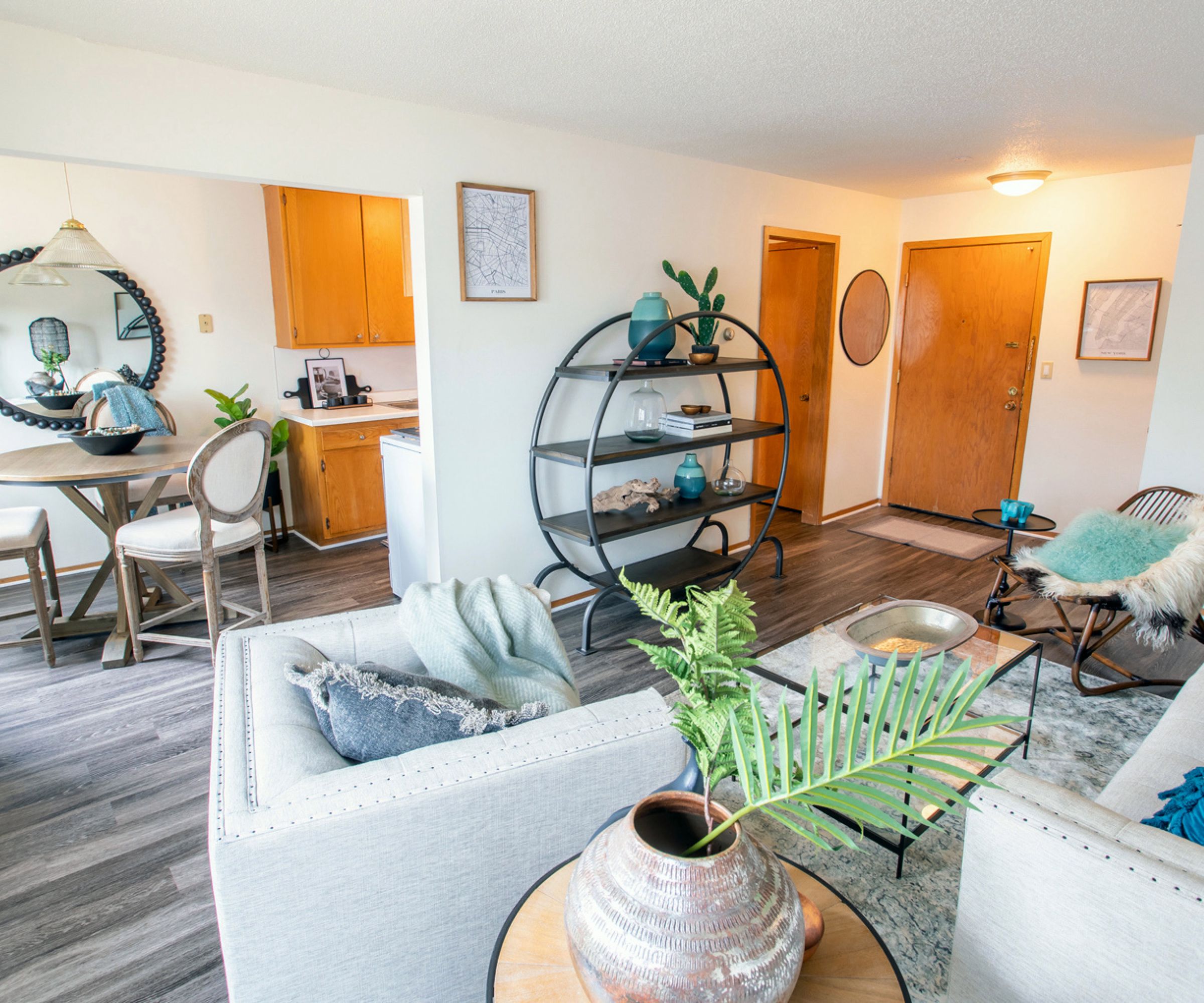 Aeon Affordable Homes Cozy living room with modern decor, a round bookshelf, and a small dining area. Neutral tones and wood floors.
