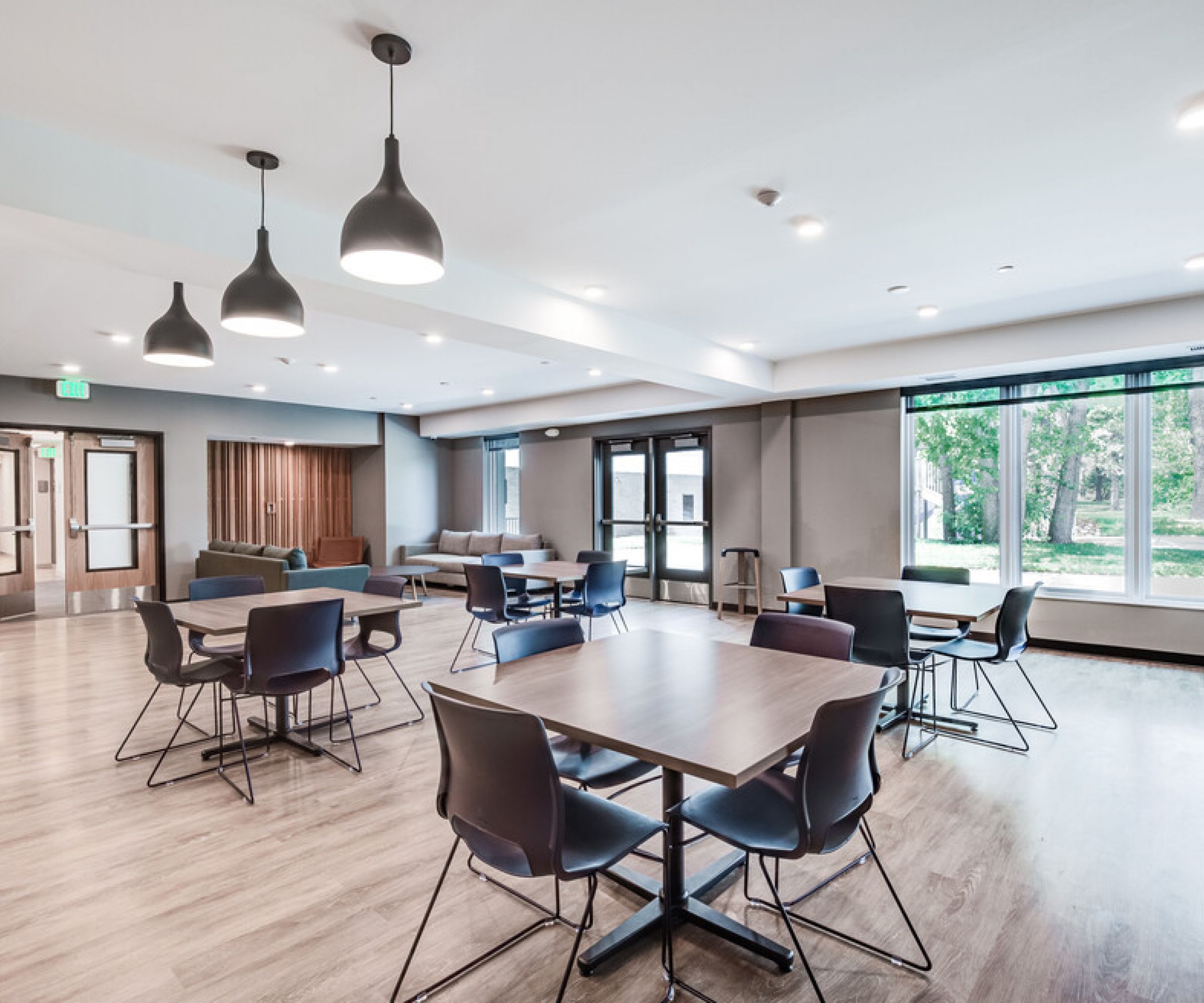 Aeon Affordable Homes and Community Modern room in affordable apartment homes with tables, chairs, pendant lights, large windows, and wooden flooring; a bright and spacious atmosphere.