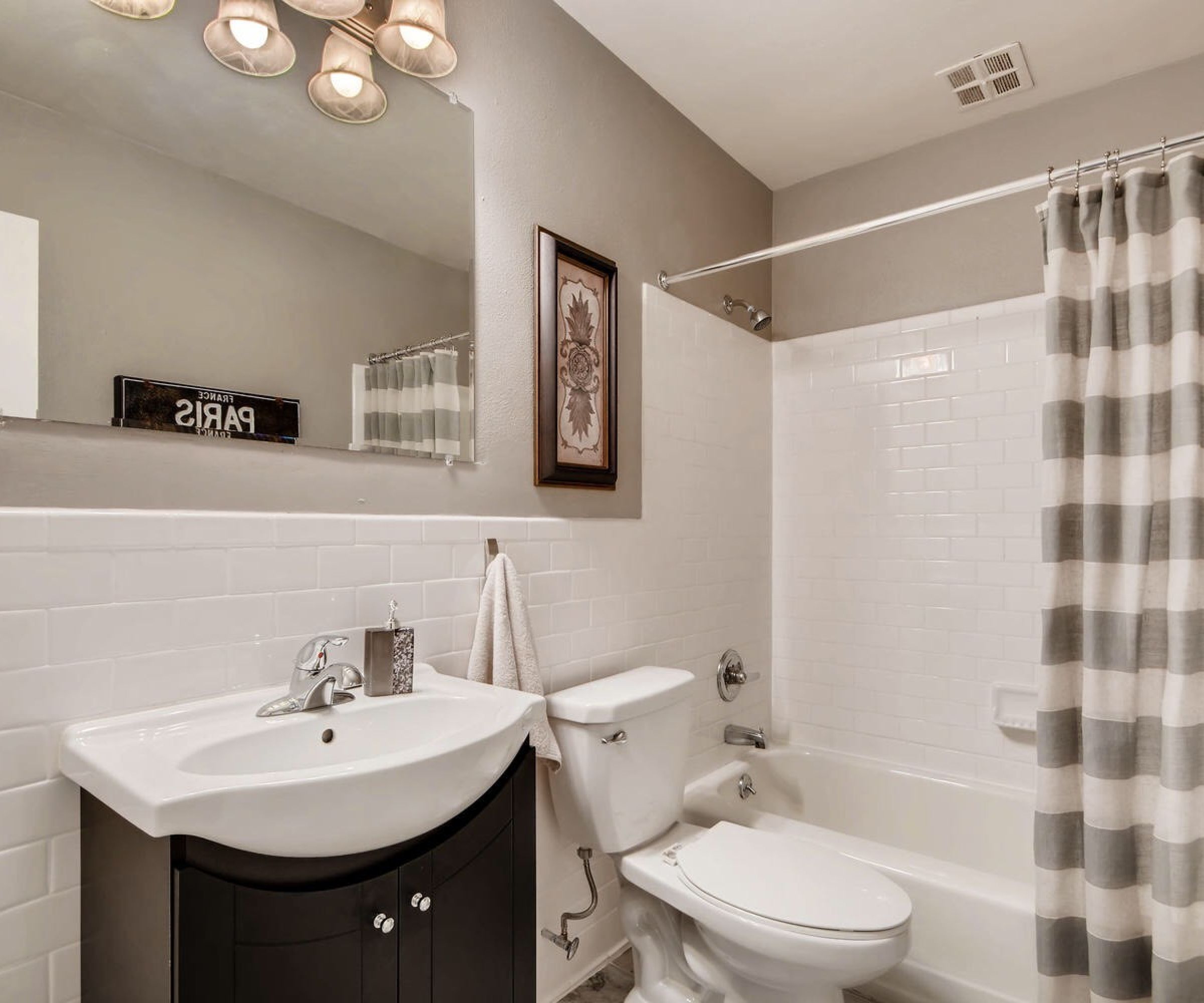 Aeon Affordable Homes and Community Modern bathroom in affordable apartment homes with white tiles, sink, toilet, and a bathtub. Gray and white striped shower curtain and wall art.