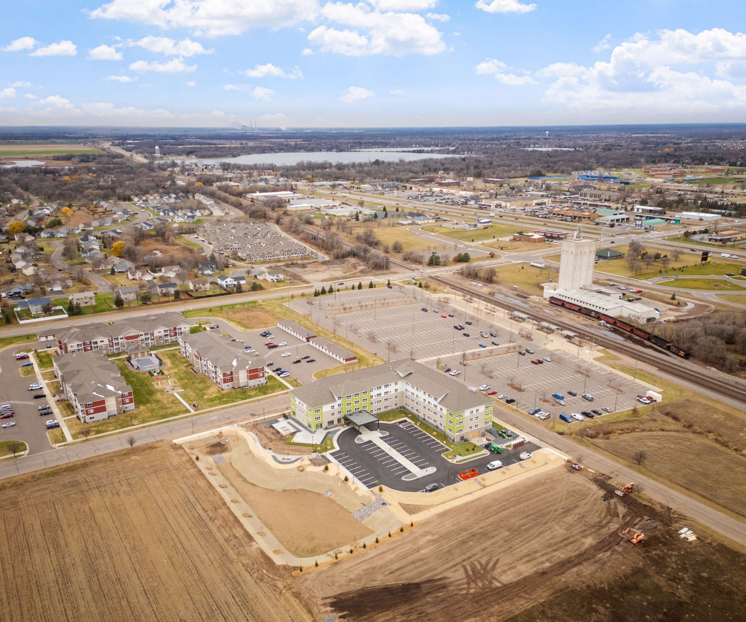 Aeon Affordable Homes and Community Aerial view of a suburban area with affordable apartment homes, residential buildings, parking lots, fields, and a railway track.