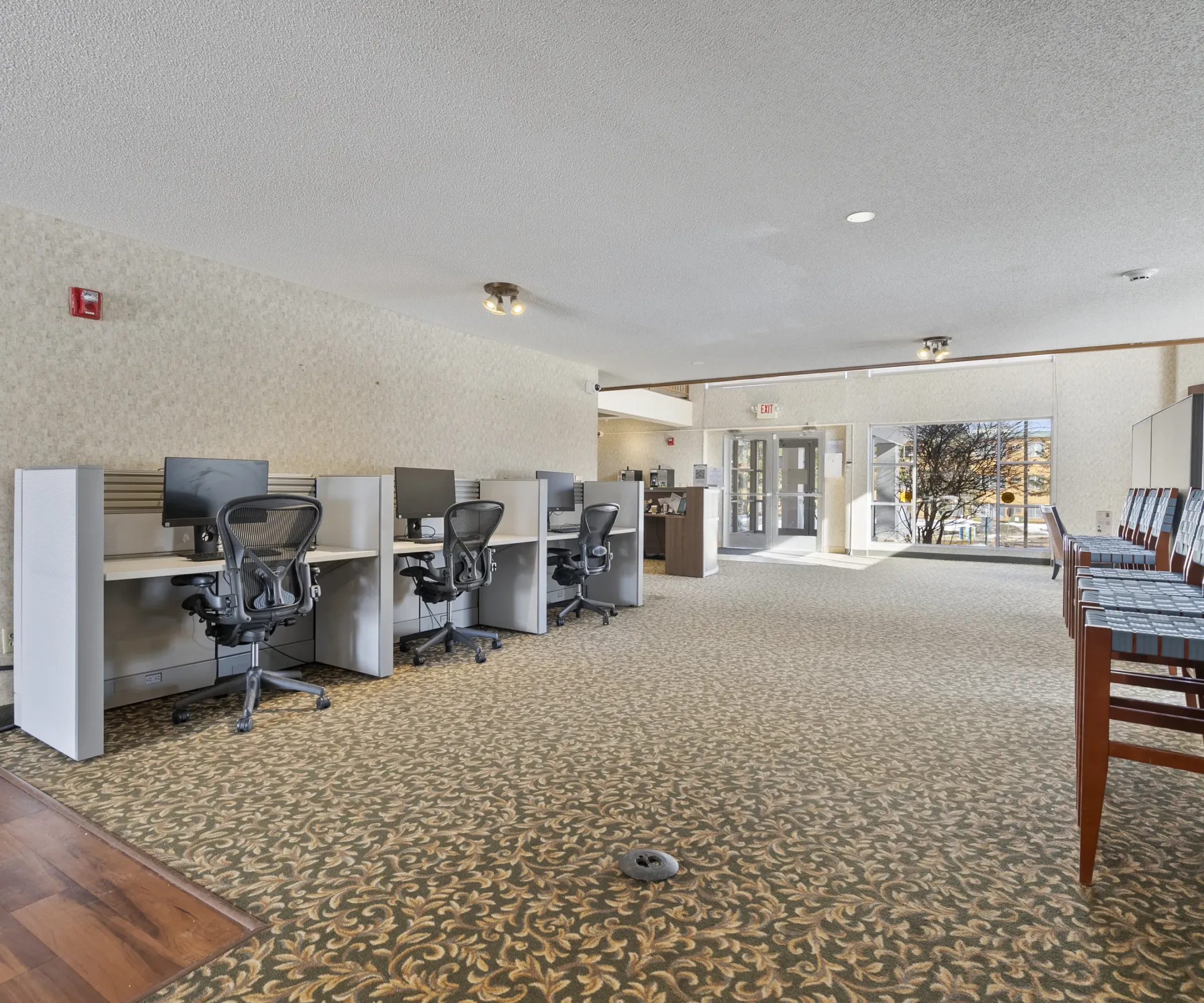 Aeon Affordable Homes Office space with several desks and chairs, patterned carpet, and natural light from large windows.