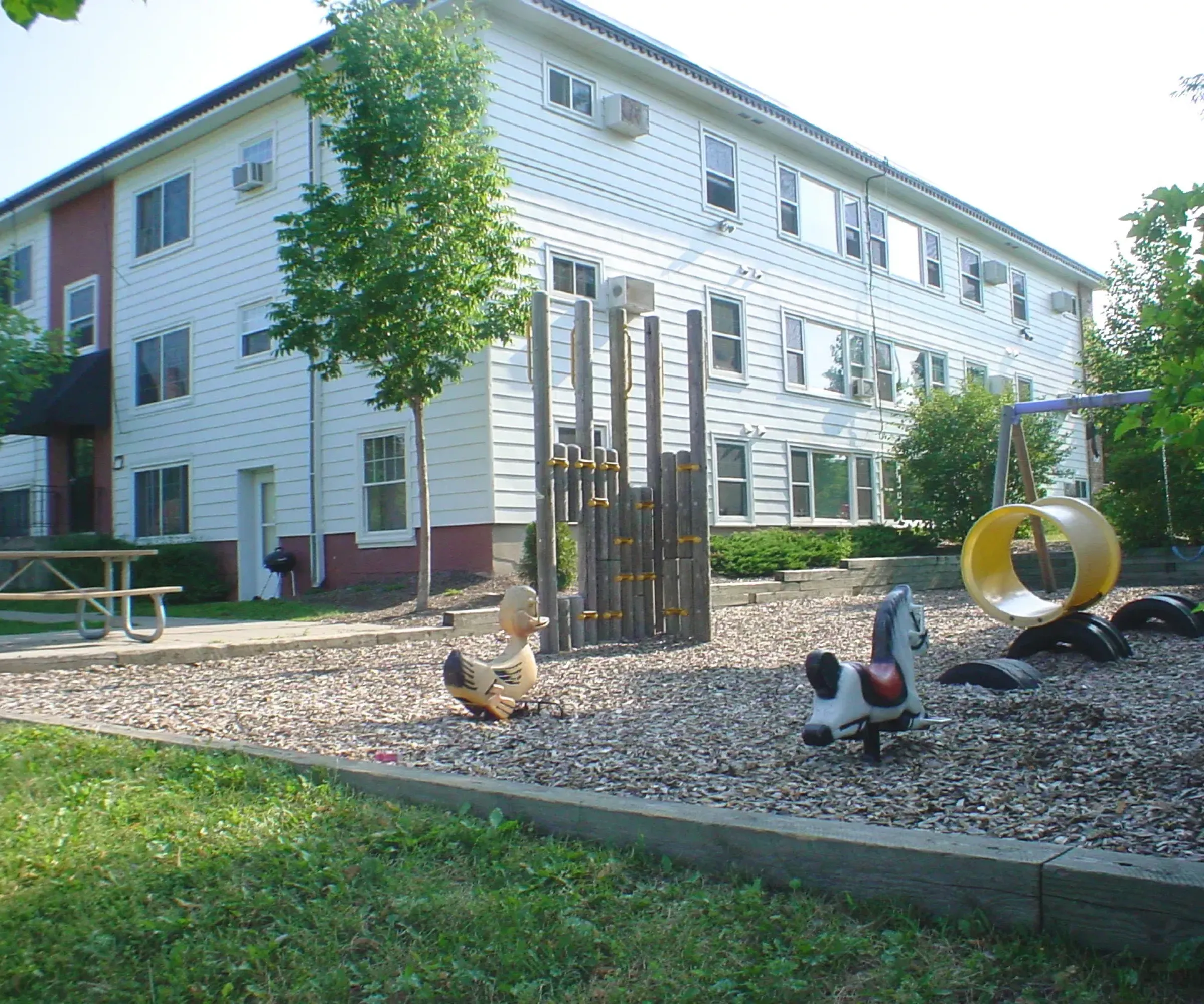 Aeon Affordable Homes and Community Affordable apartment homes stand near the playground with climbing structures and animal spring riders, perfect for family fun.