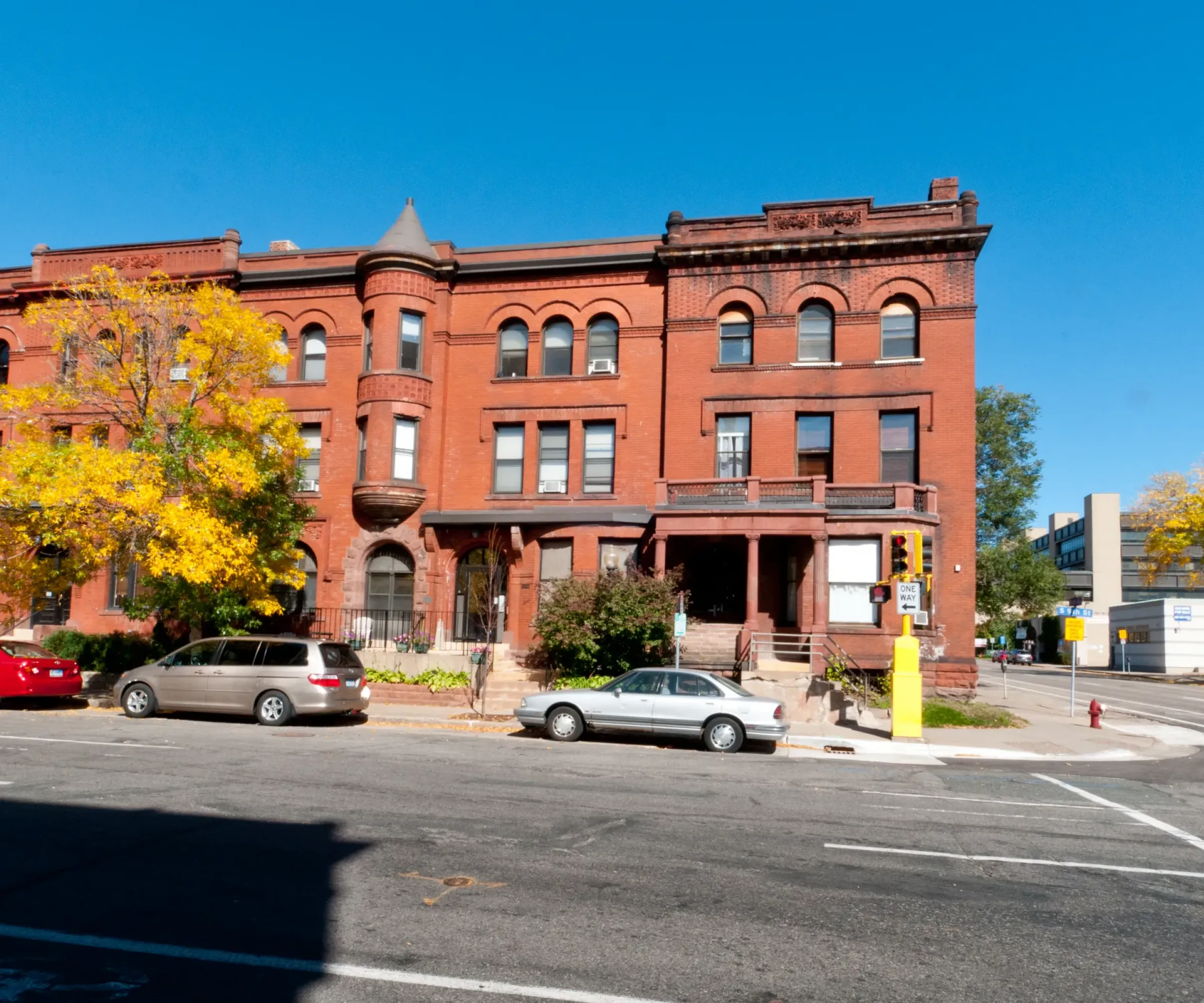 Aeon Affordable Homes and Community Affordable apartment homes nestled in a historically-styled red brick building with arched windows and trees with yellow leaves under a clear blue sky.