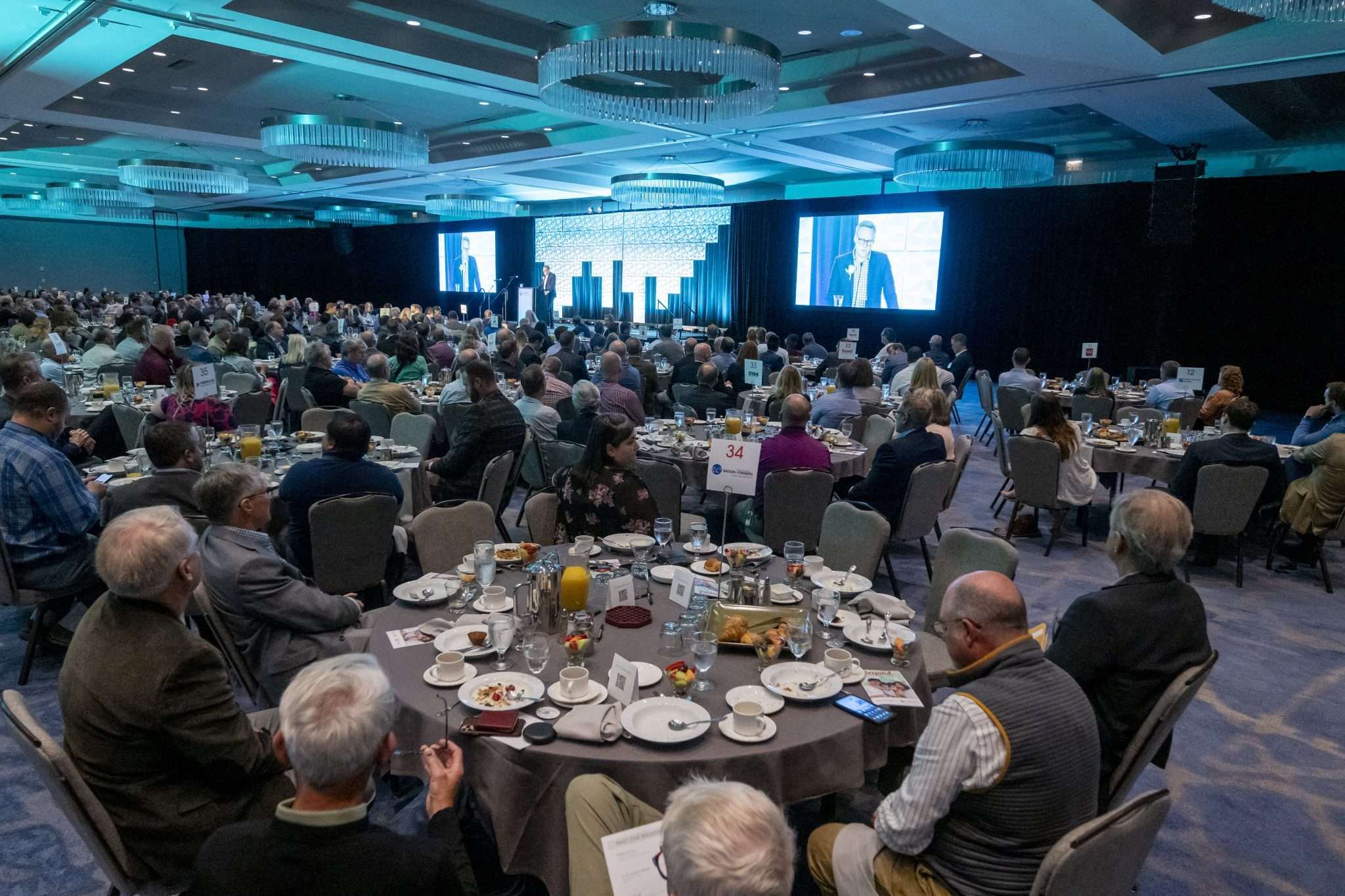 Aeon Affordable Homes and Community A large conference room filled with seated attendees watching a speaker on stage and on screens.