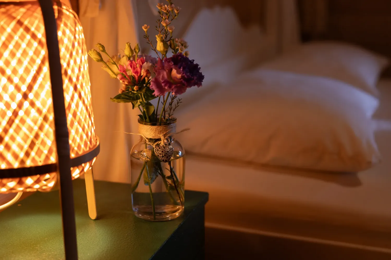 Aeon Affordable Homes with a cozy bedroom scene, a glowing lamp, a vase of colorful flowers, and a neatly made bed in soft lighting.