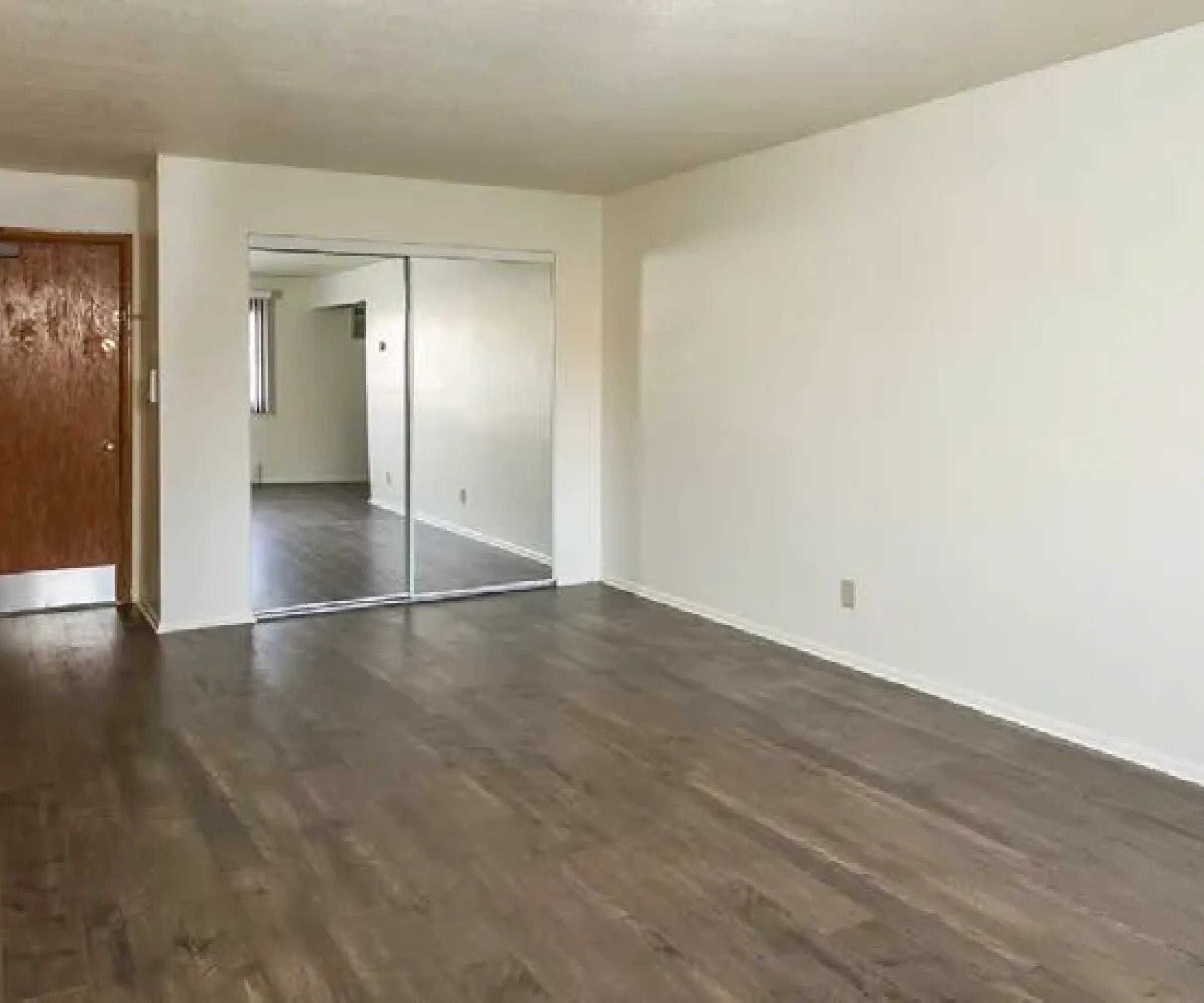 Aeon Affordable Homes Empty room with wooden floor, white walls, a mirrored closet, and a wooden door in the corner at Cobblestone Court Apartments.