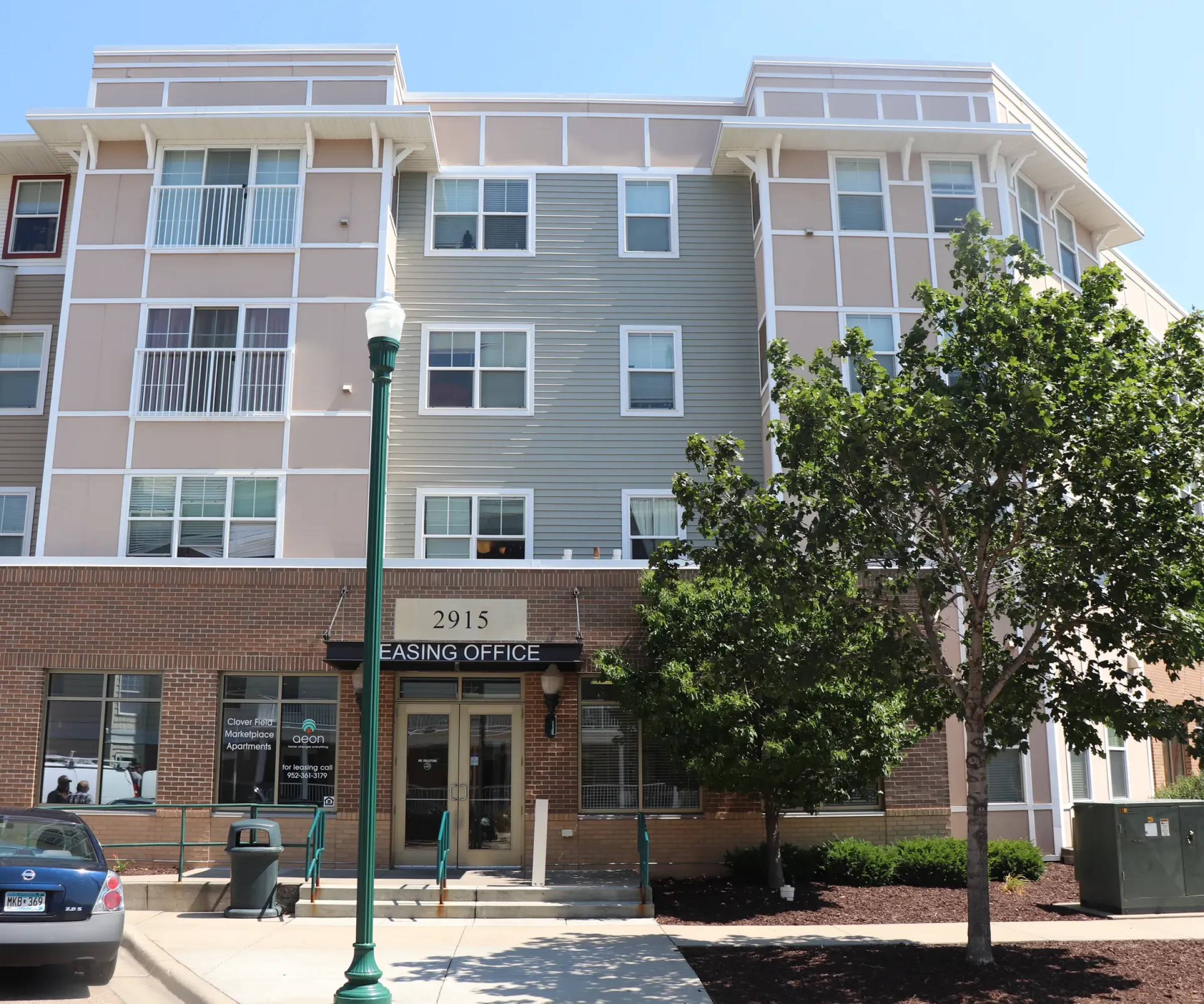Aeon Affordable Homes and Community Affordable apartment homes with a leasing office entrance, ample parking, and green leafy trees enhancing the front view.