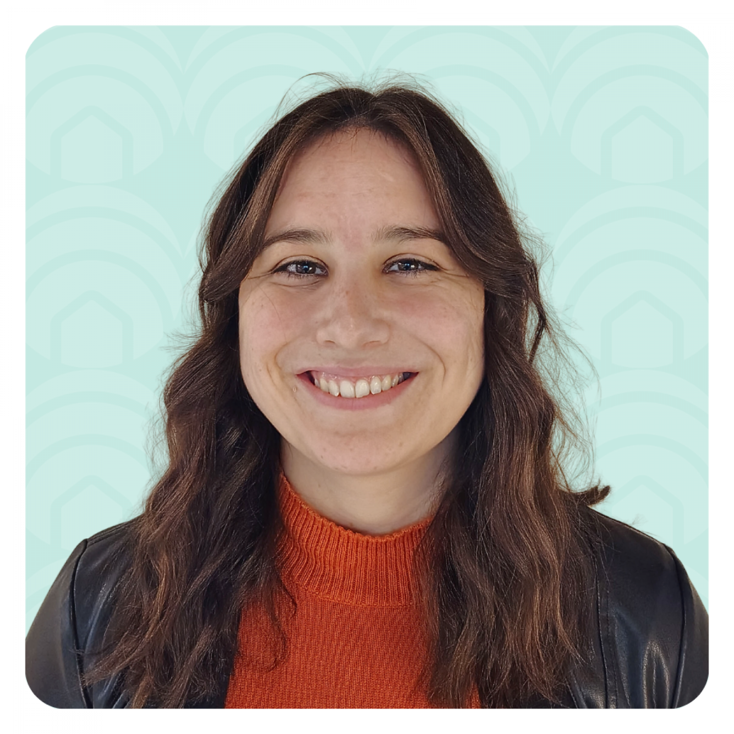 Aeon Affordable Homes Smiling woman with wavy brown hair in an orange sweater and black jacket, against a light blue patterned background.
