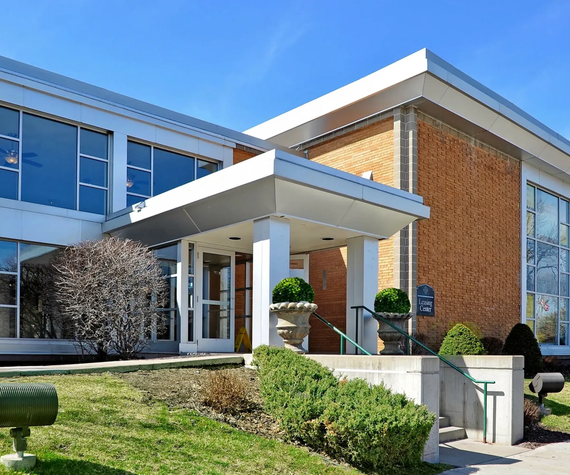 Aeon Affordable Homes Single-story brick building with glass entrance and landscaped greenery.