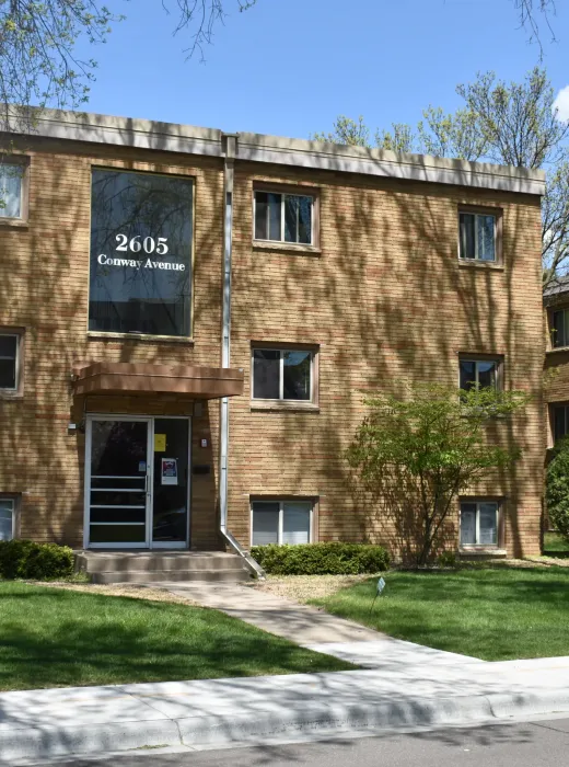 Aeon Affordable Homes The Cobblestone Court Apartments boast a three-story brick design, surrounded by a lush lawn and towering trees.
