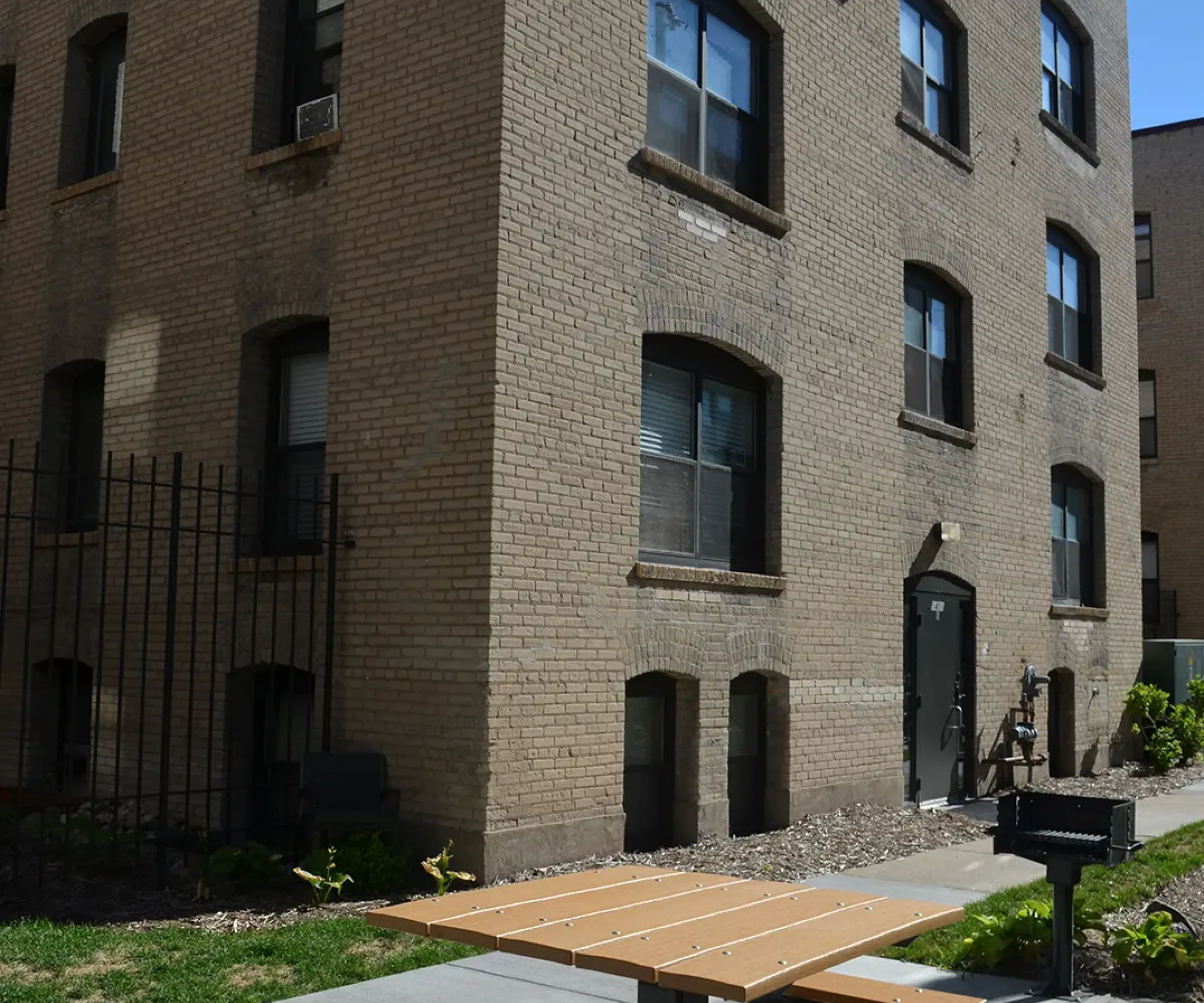Aeon Affordable Homes and Community A brown brick apartment building offers affordable apartment homes with a courtyard featuring a picnic table and barbecue grill.