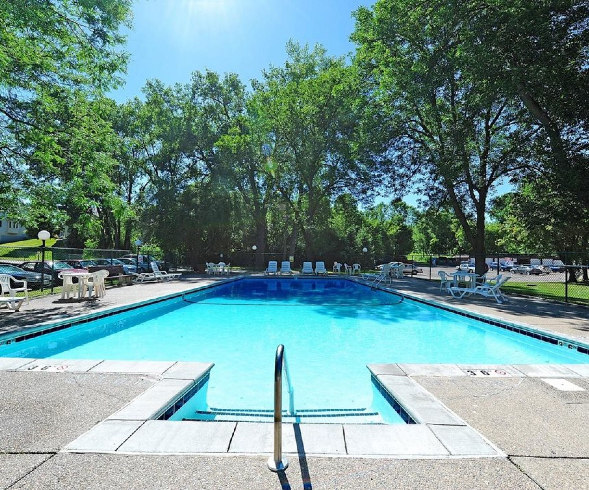 Aeon Affordable Homes and Community Affordable apartment homes featuring an outdoor swimming pool, surrounded by trees with lounge chairs and tables for sunny relaxation.