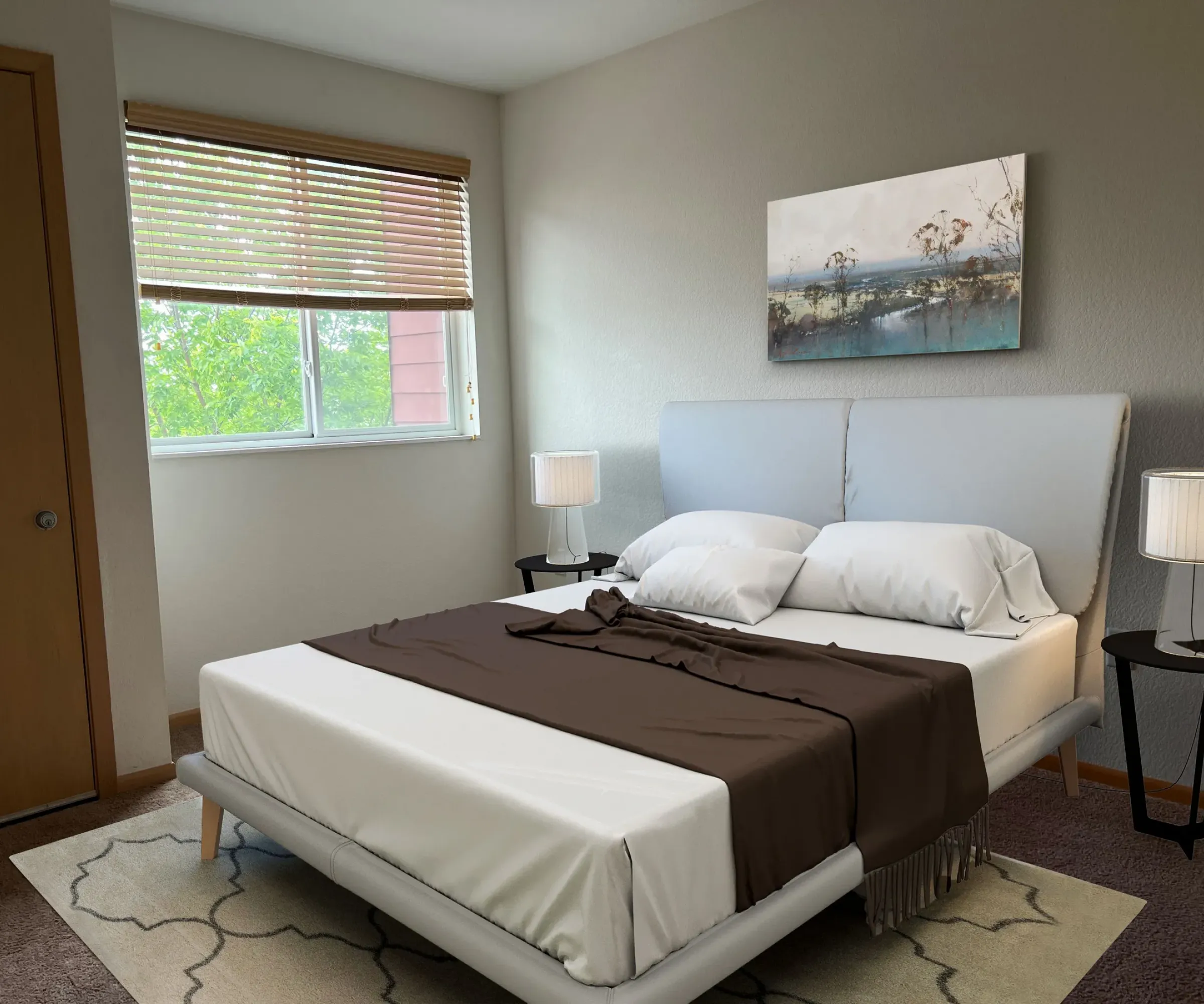 Aeon Affordable Homes and Community A modern bedroom in affordable apartment homes features a bed, brown throw blanket, bedside tables with lamps, and a landscape painting.