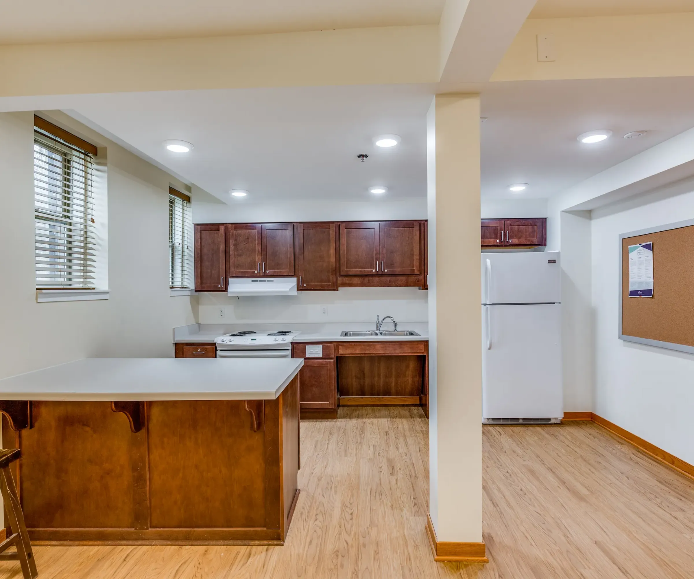 Aeon Affordable Homes and Community A modern kitchen in affordable apartment homes with wooden cabinets, a white fridge, stove, and a breakfast bar with a stool.