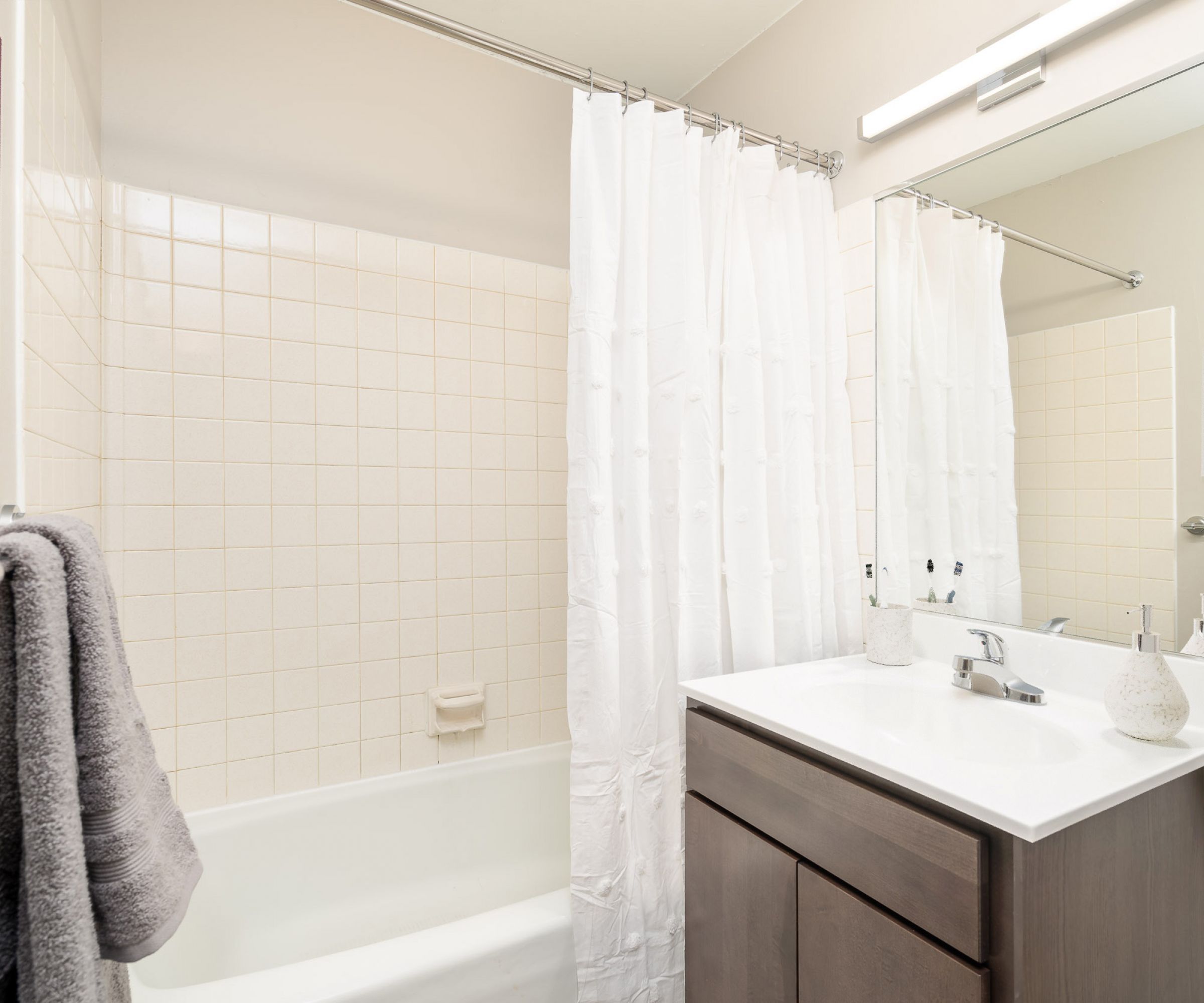 Aeon Affordable Homes and Community Modern bathroom in affordable apartment homes featuring a white shower curtain, tiled walls, a mirror, and a wooden vanity with a white countertop.