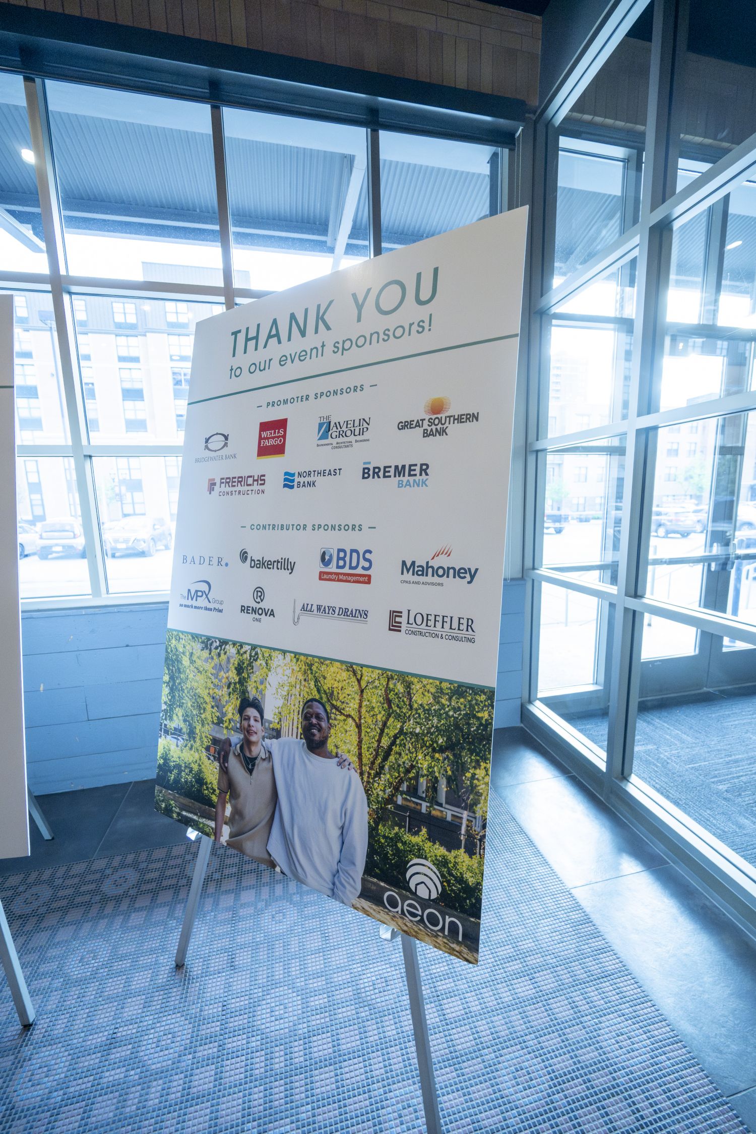 Aeon Affordable Homes Event sponsor sign on an easel, featuring logos and a family photo at the bottom.