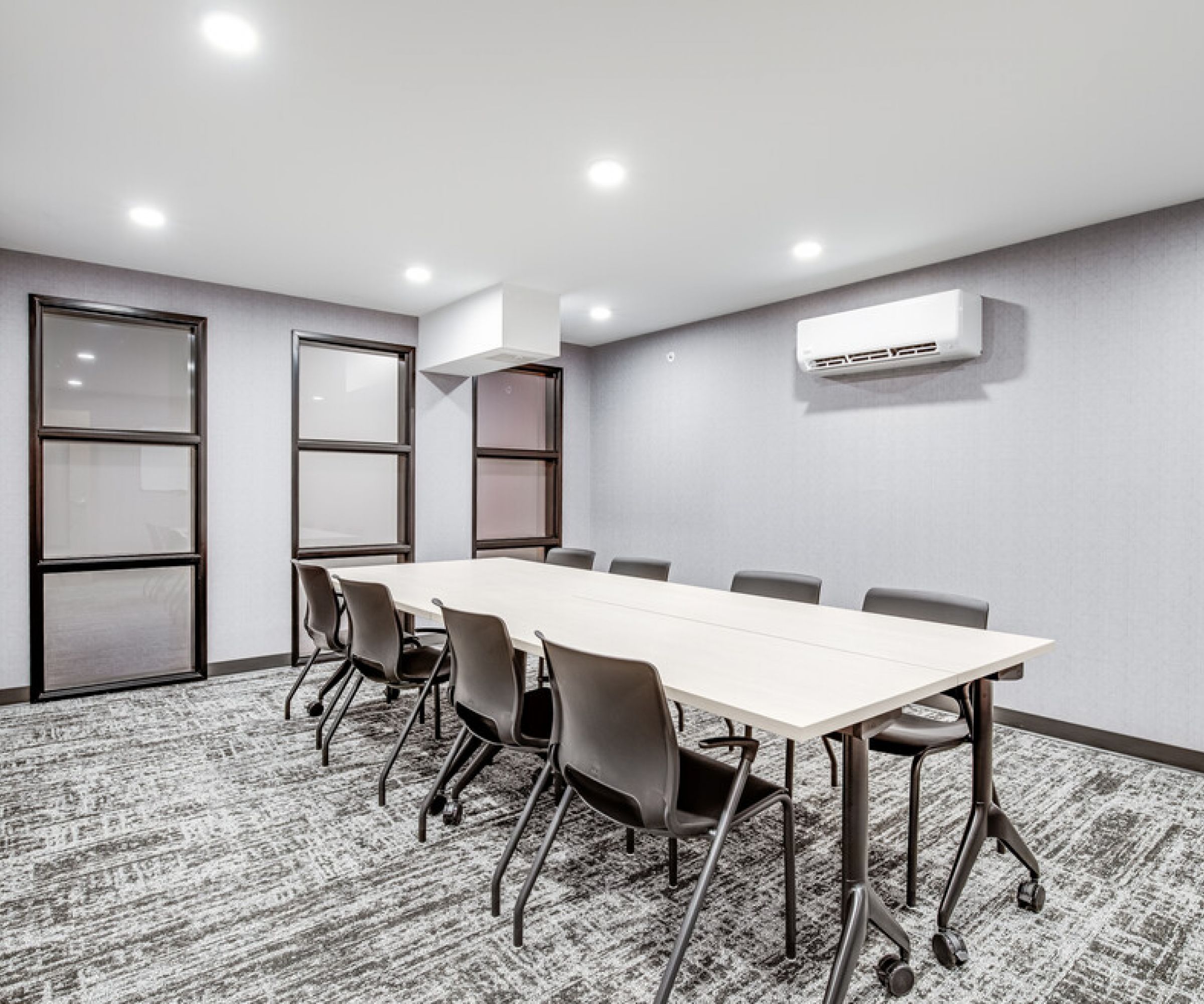 Aeon Affordable Homes and Community Minimalist conference room in affordable apartment homes with a long table, six black chairs, gray walls, carpet, and bright ceiling lights.
