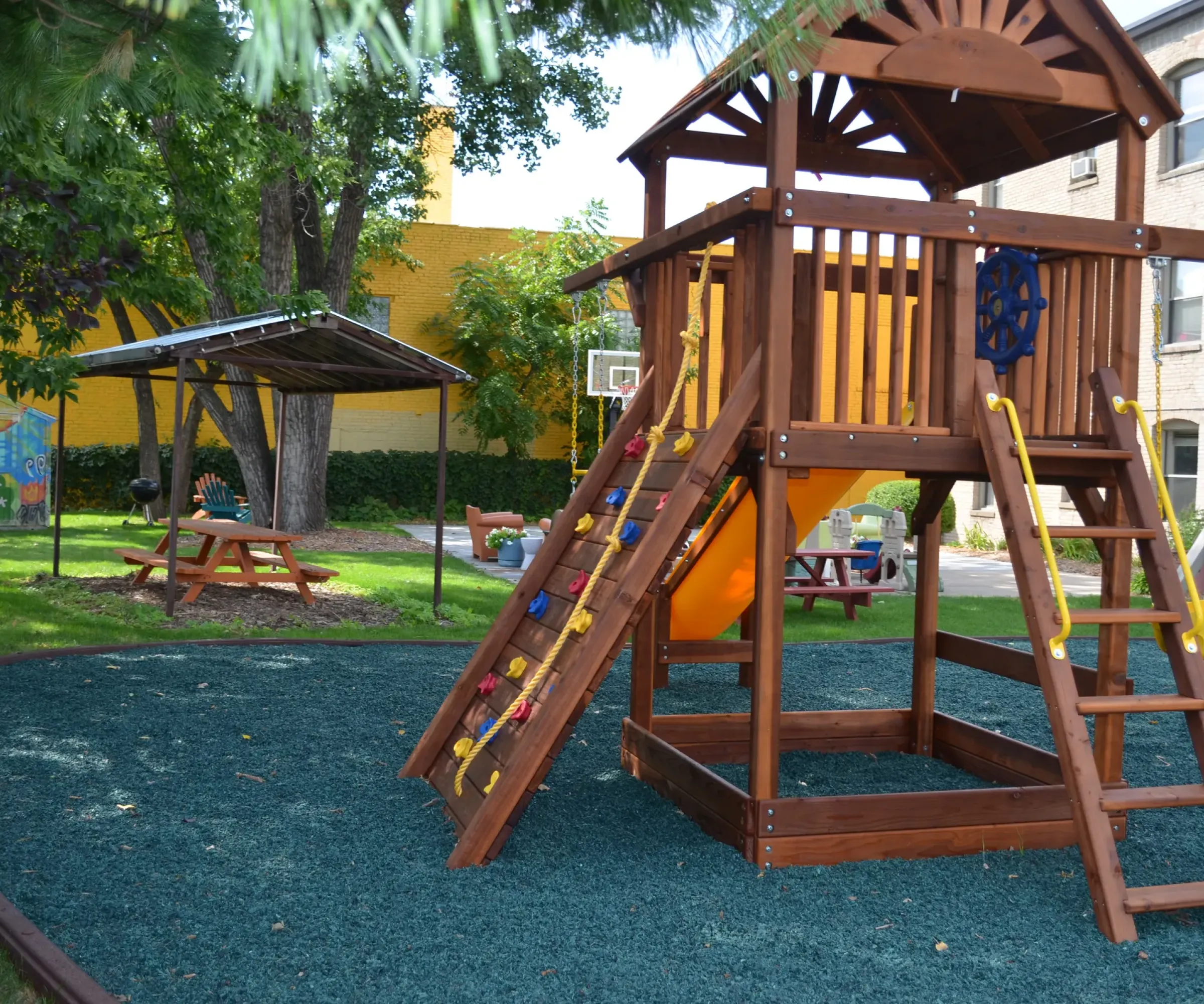 Aeon Affordable Homes and Community Wooden playground structure with slide and climbing wall on a cushioned surface, like those found near affordable apartment homes.