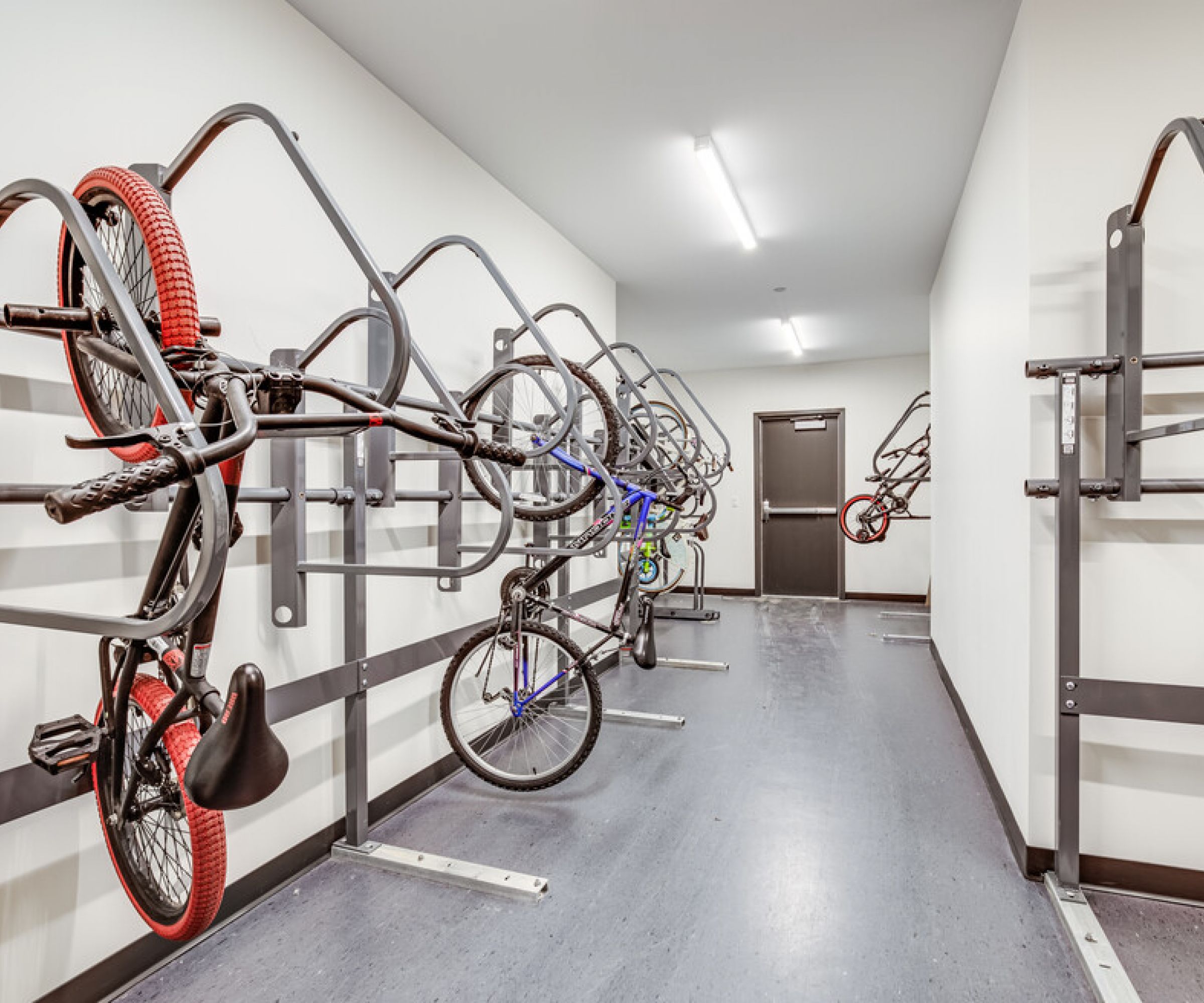 Aeon Affordable Homes and Community Affordable apartment homes with sleek hallways feature bicycles hanging on vertical racks against white walls and gray flooring.