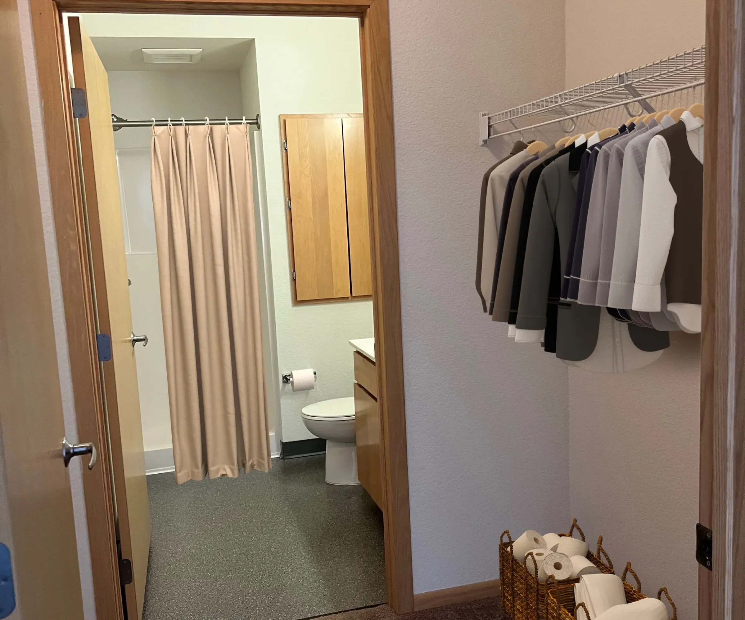 Aeon Affordable Homes and Community A cozy, affordable apartment home with a closet full of suits and a bathroom featuring a shower curtain, toilet, mirror, and floor baskets.