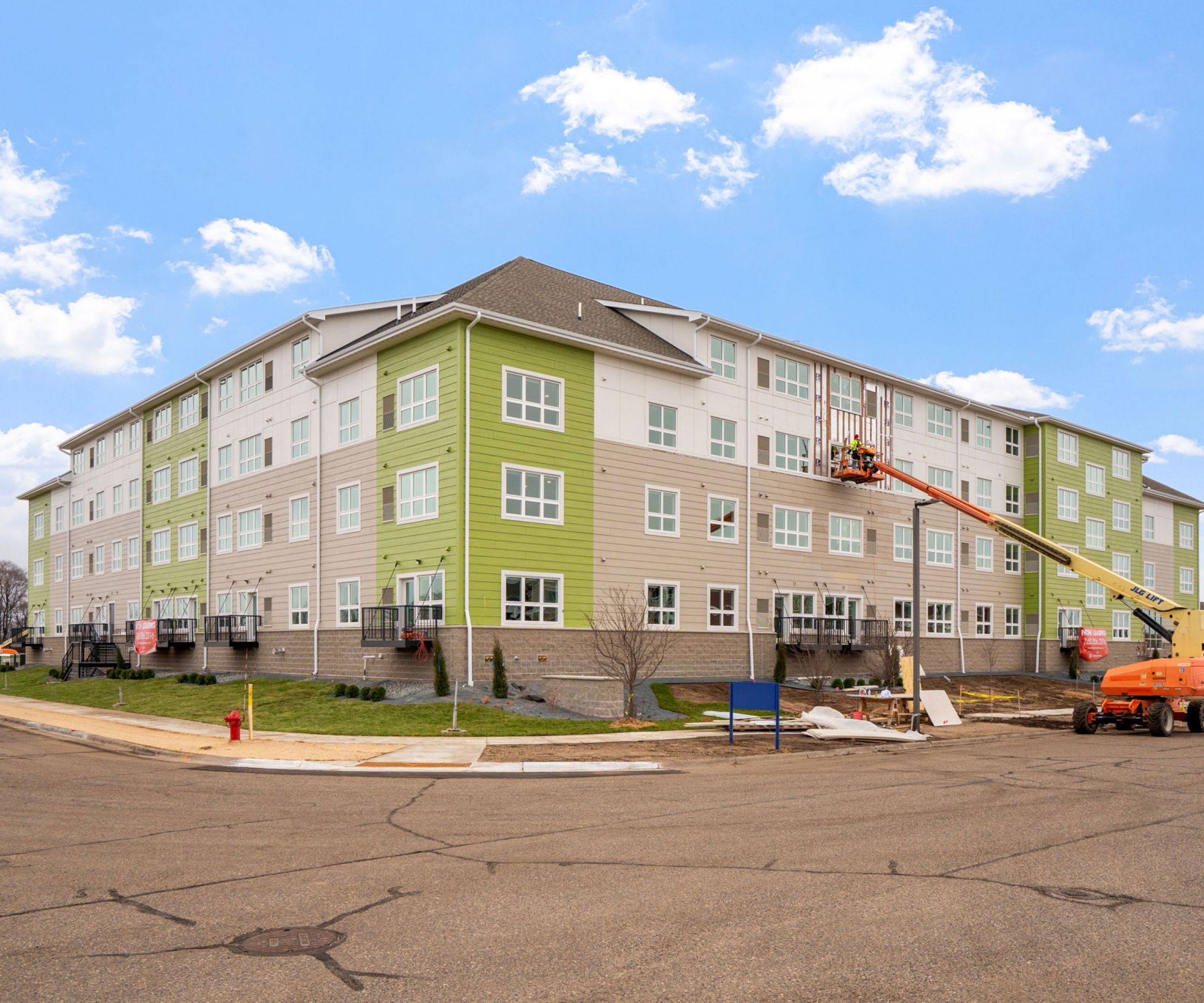 Aeon Affordable Homes and Community Four-story building with a green and beige facade under construction, offering affordable apartment homes, features a cherry picker lift in the foreground.
