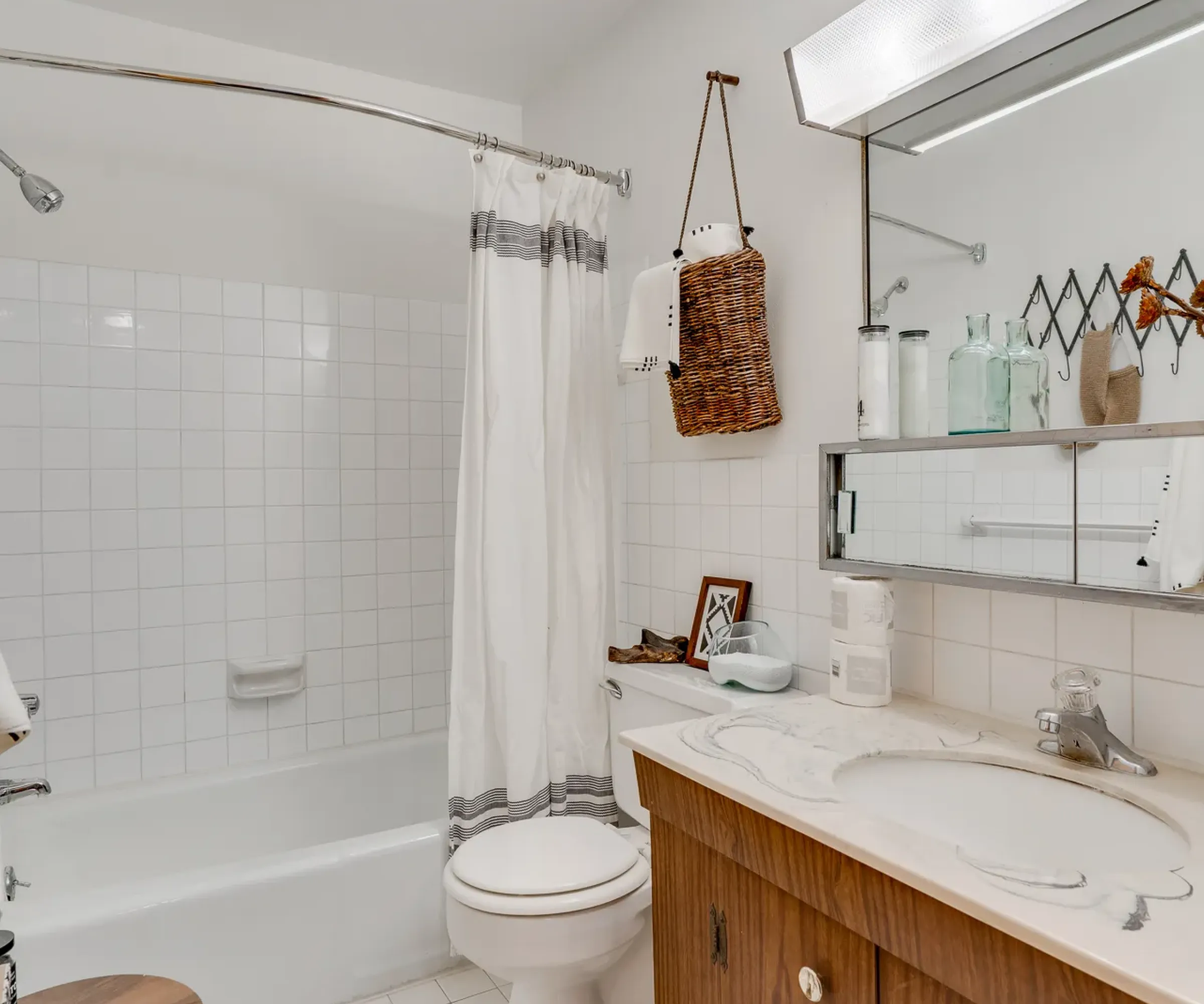 Aeon Affordable Homes Bathroom with a white tub, curtain, wooden vanity, large mirror, and striped rug on tiled floor.
