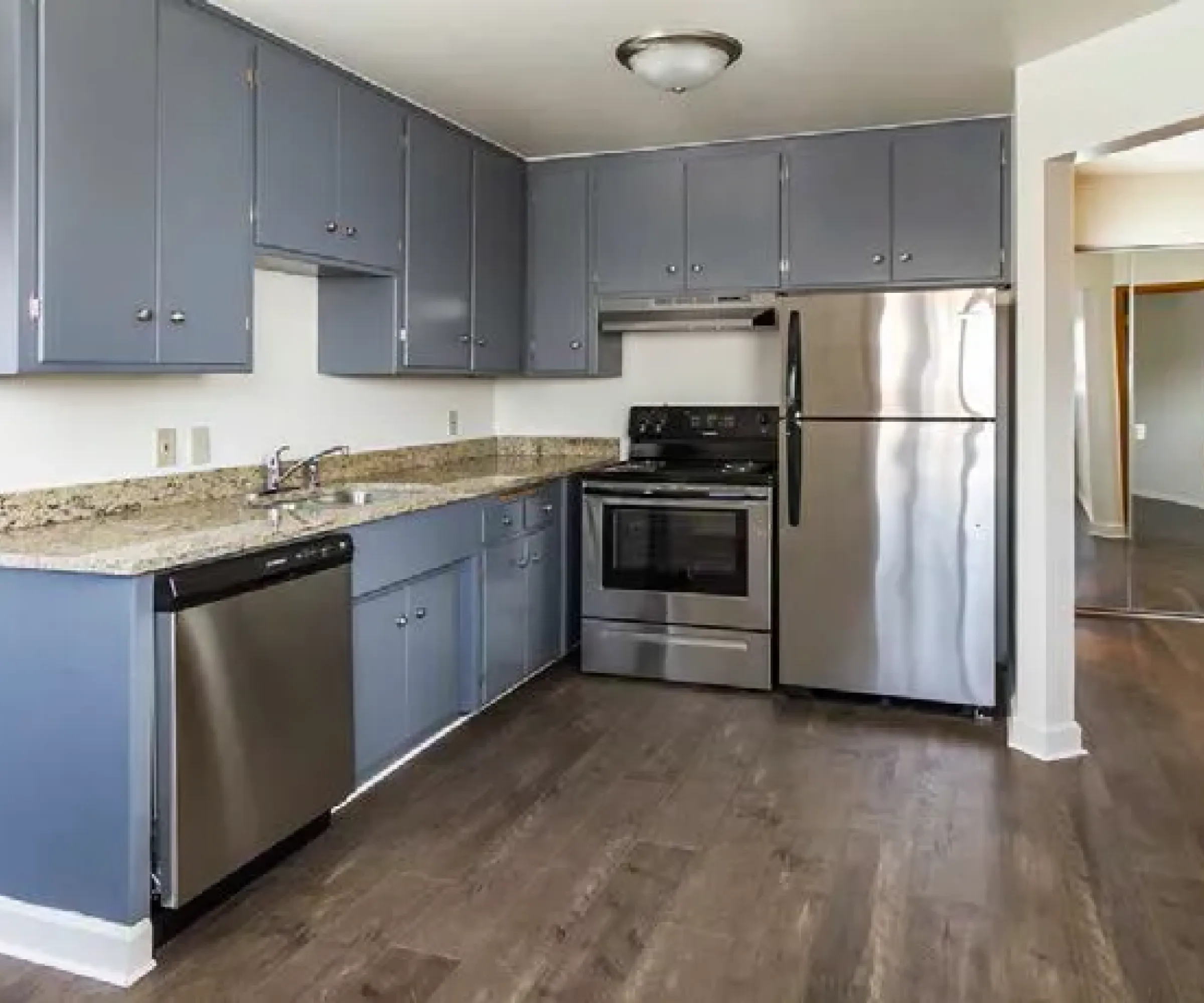 Aeon Affordable Homes Modern kitchen at Cobblestone Court Apartments featuring blue cabinets, stainless steel appliances, granite countertops, and wood flooring.