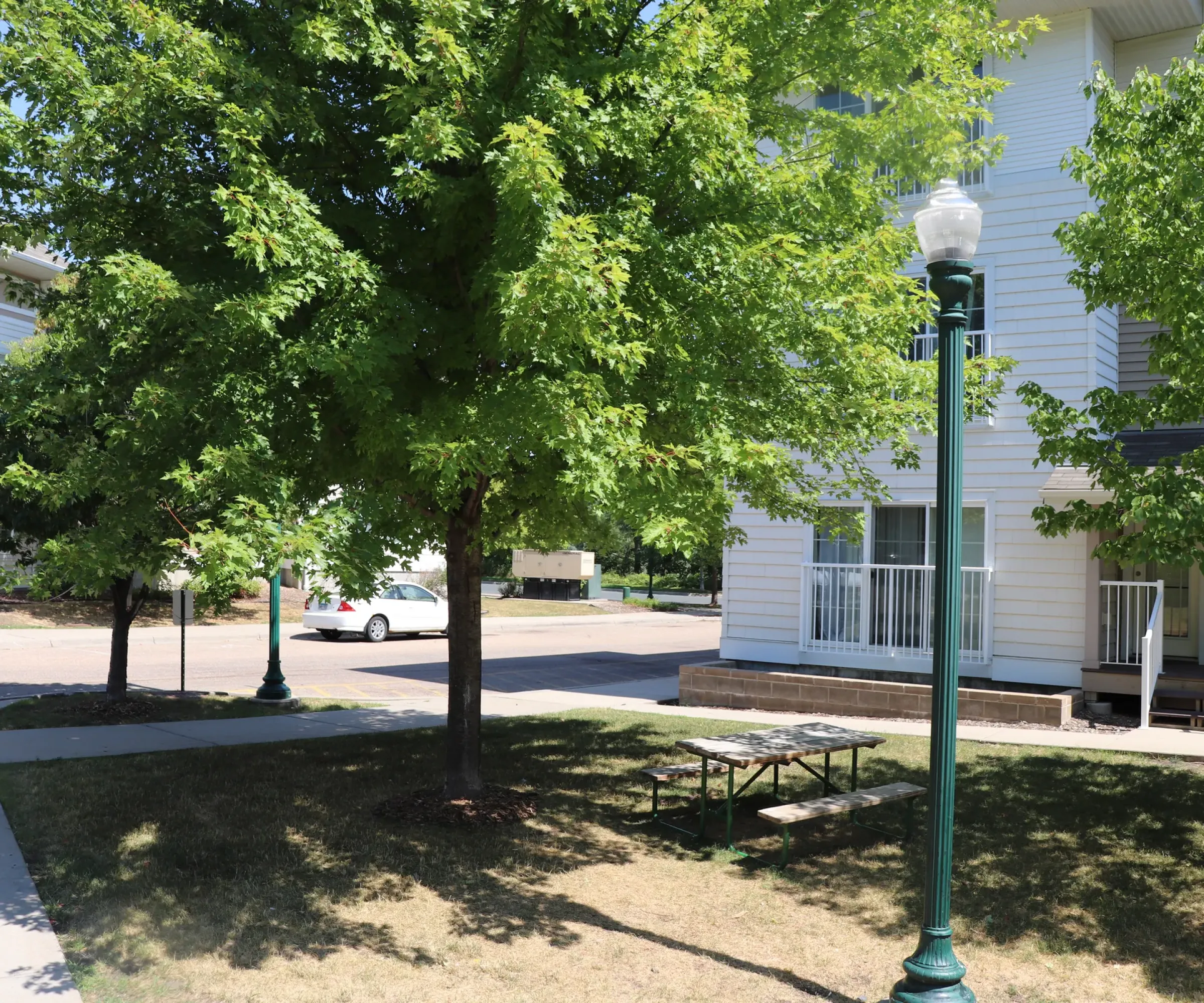 Aeon Affordable Homes and Community A picnic table under a tree beside an affordable apartment home on a sunny day.