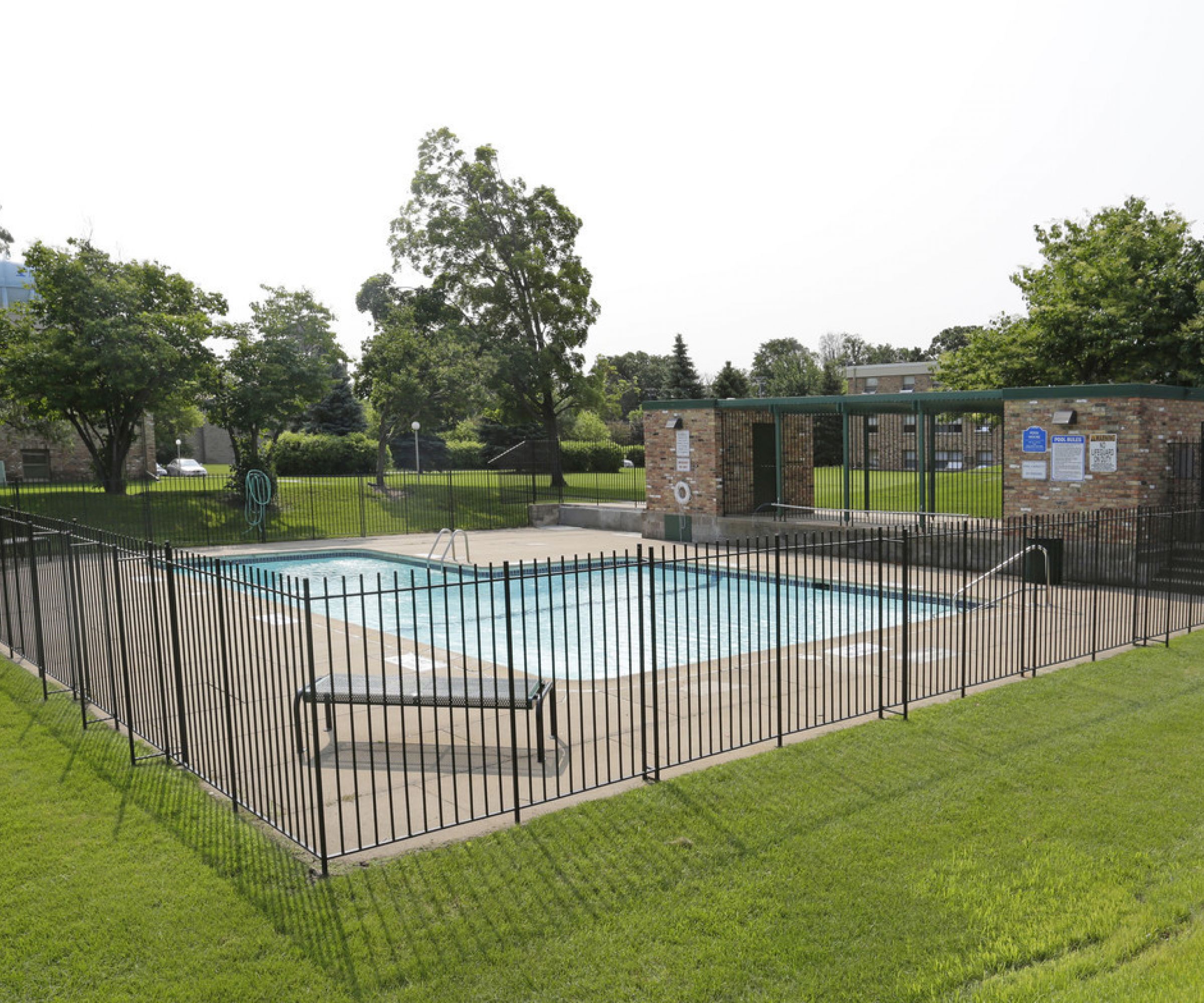 Aeon Affordable Homes and Community Fenced outdoor pool with stone entry, nestled within grassy lawns and trees, ideal for affordable apartment homes.