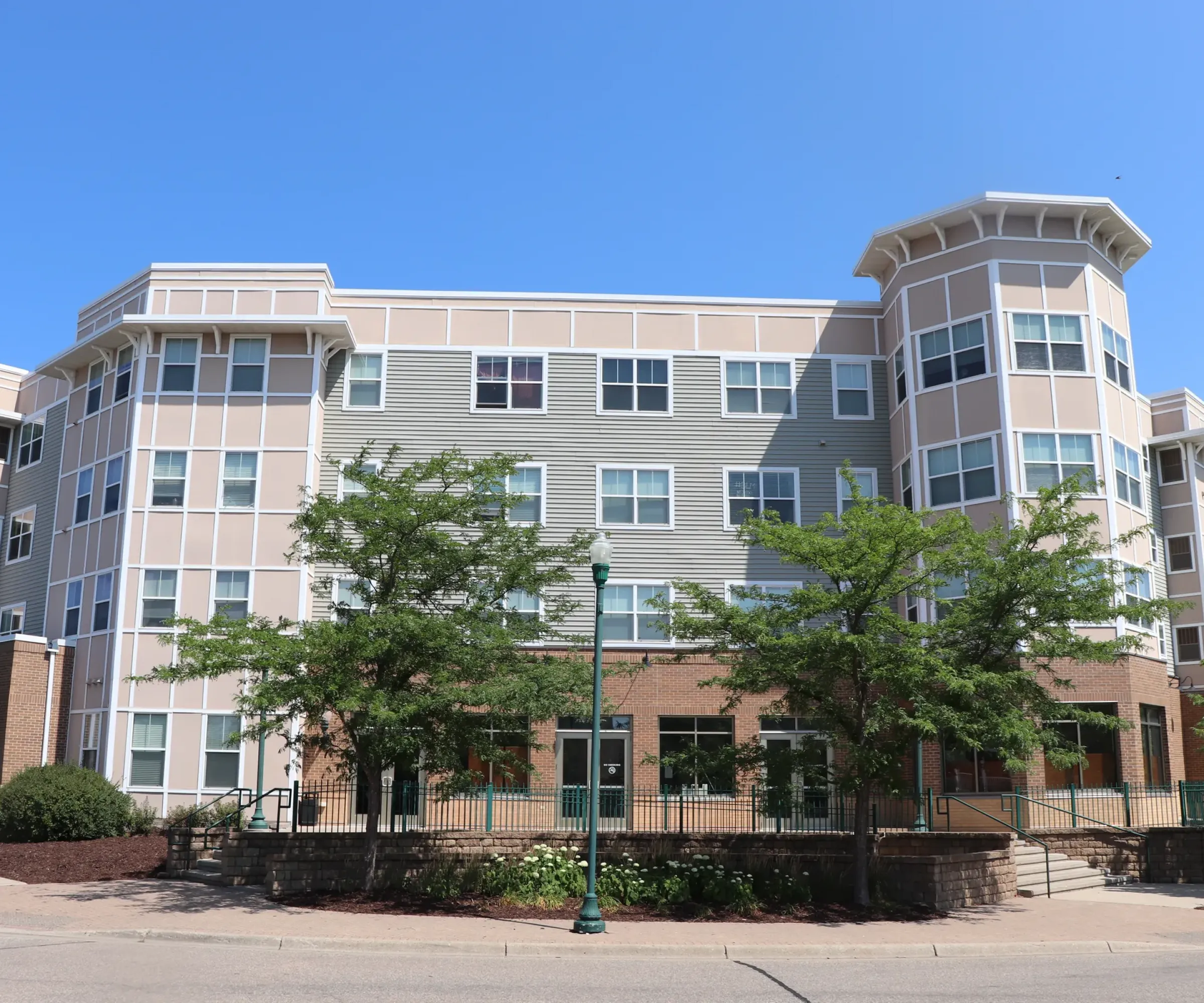 Aeon Affordable Homes and Community Affordable apartment homes in a modern building with trees in front and a clear blue sky backdrop.