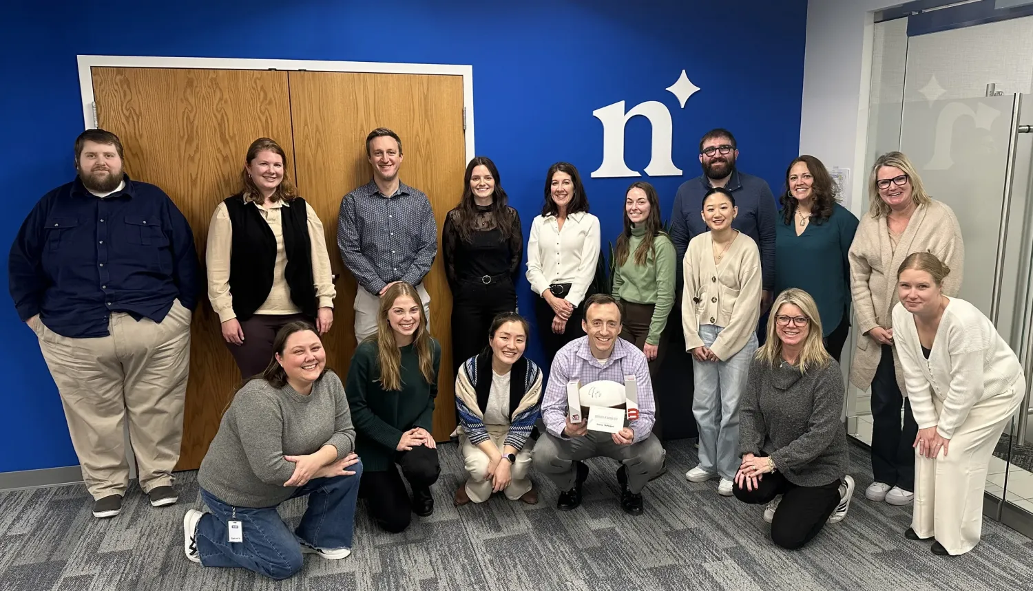 Aeon Affordable Homes Group of people smiling and posing indoors in front of a blue wall with a white "n" logo.