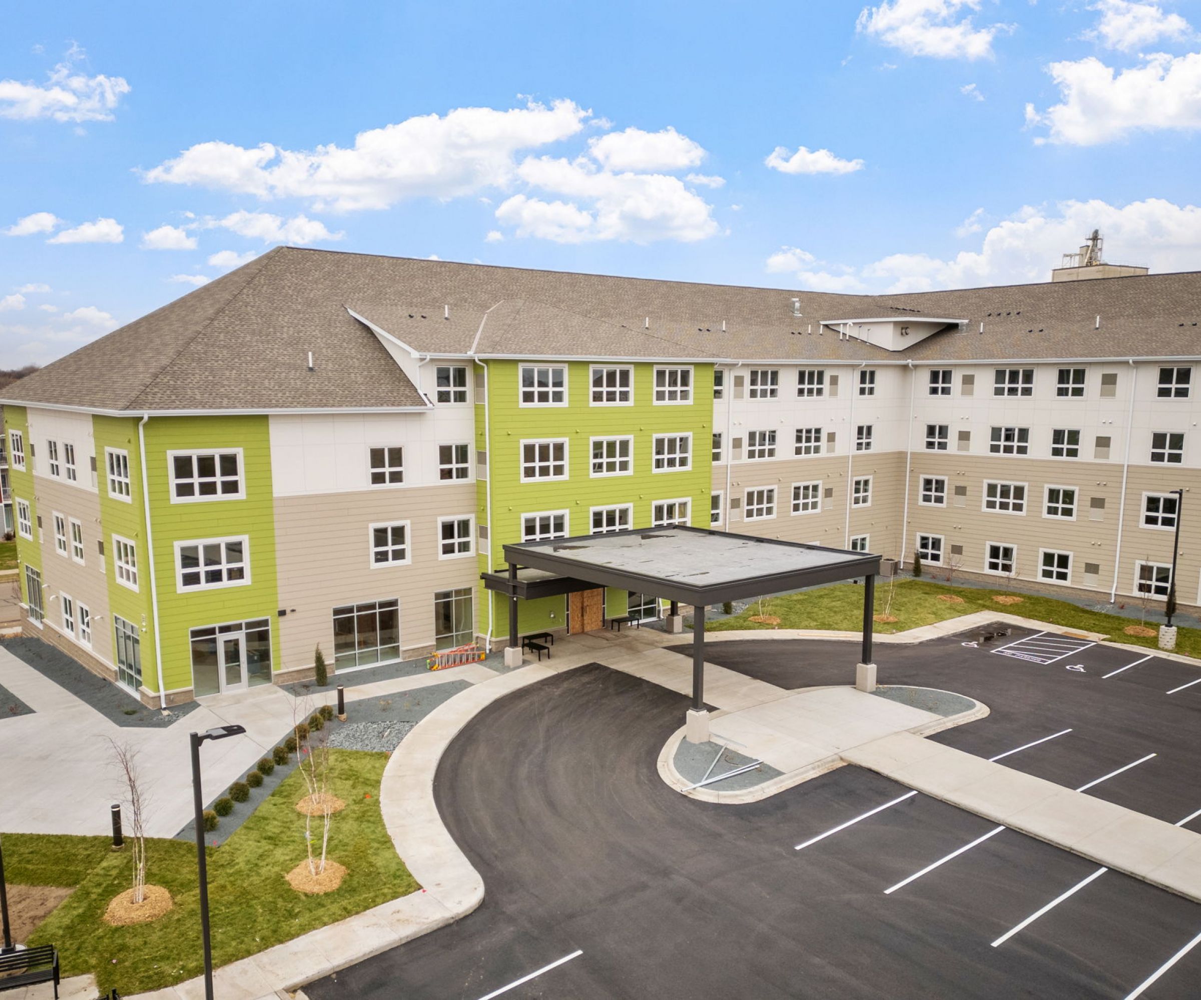 Aeon Affordable Homes and Community A large, modern apartment building with a covered entrance and adjacent parking lot offers affordable apartment homes under a blue sky.