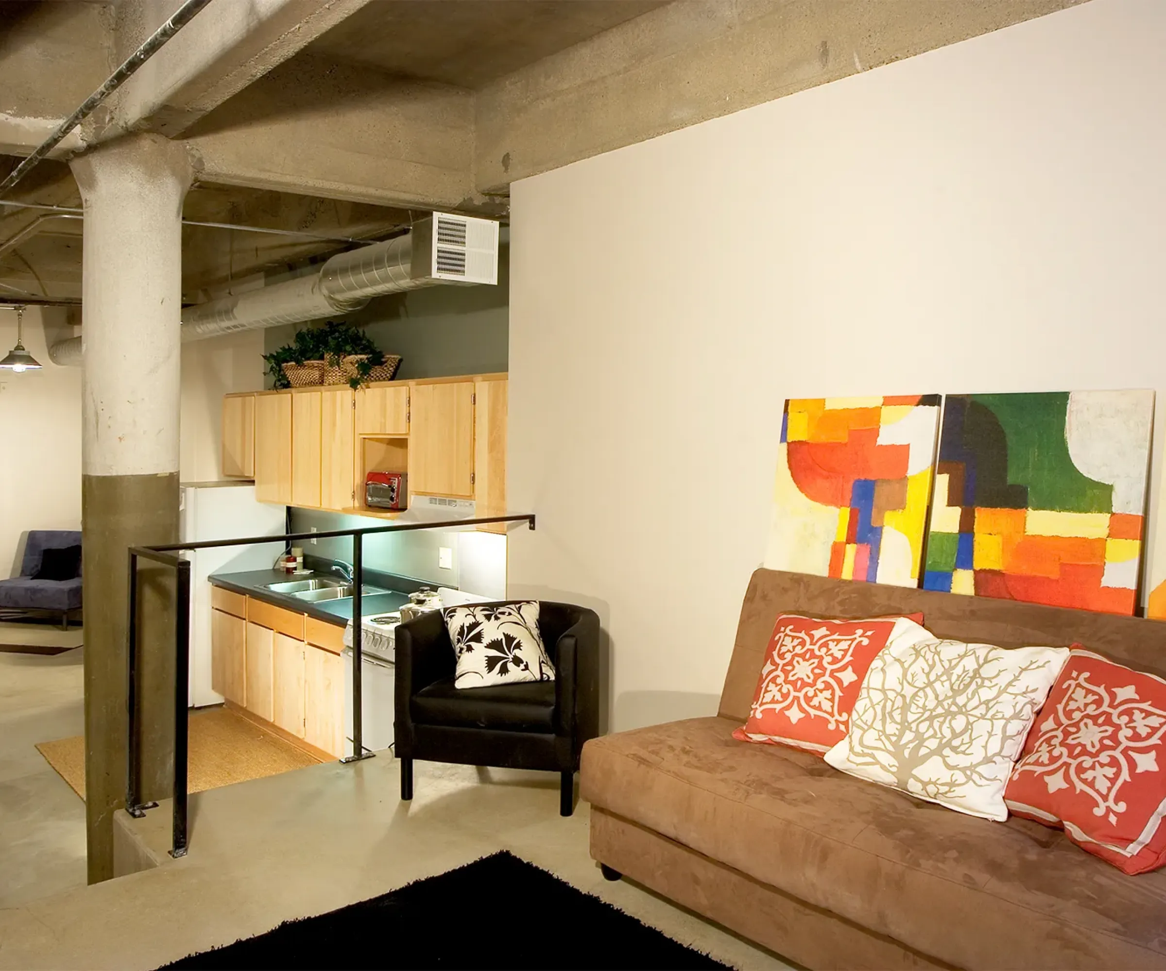 Aeon Affordable Homes and Community Affordable apartment homes with a modern loft vibe, featuring colorful abstract art, a brown couch with vibrant pillows, and a quaint wooden kitchen area.