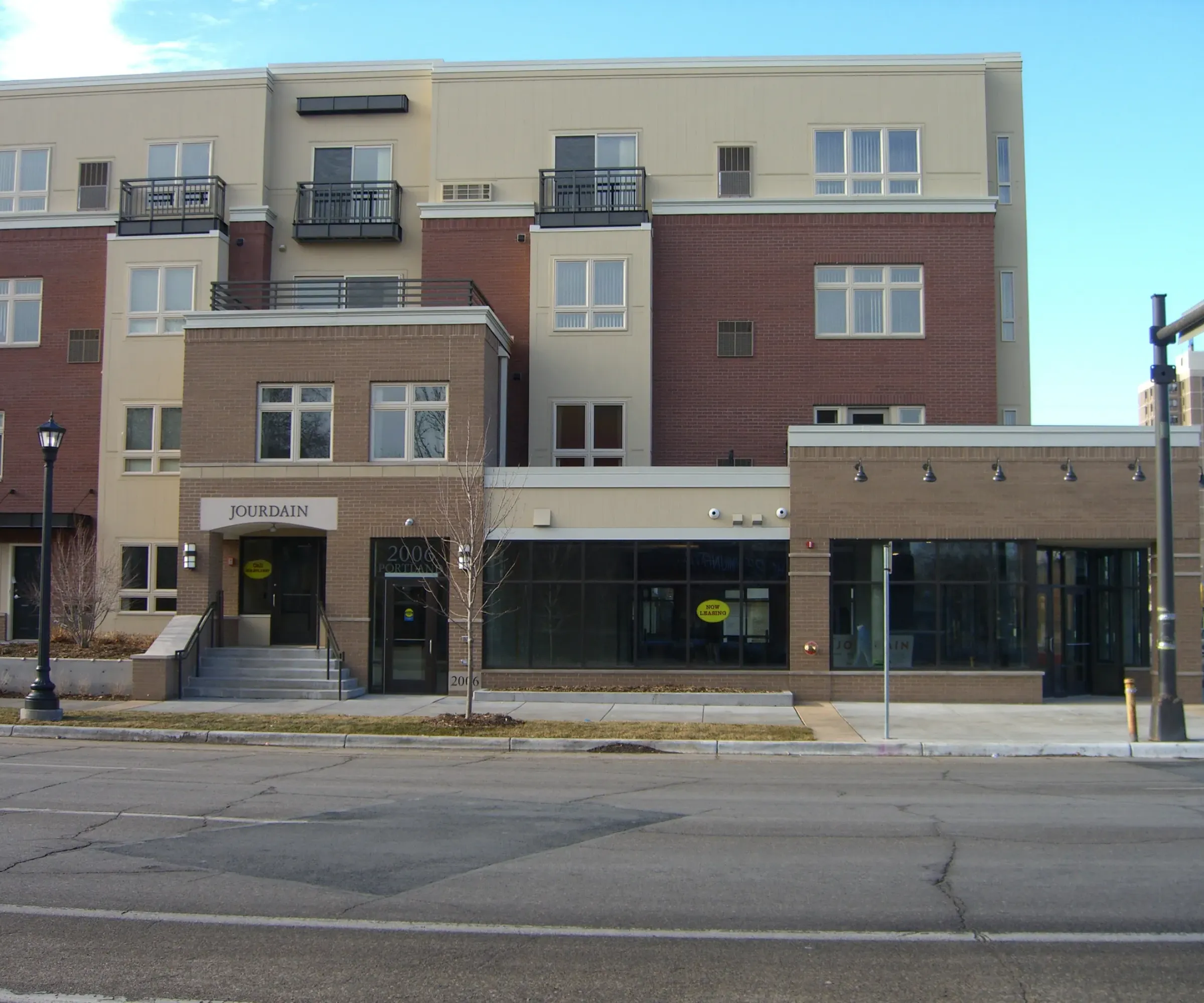 Aeon Affordable Homes and Community Three-story brick and cream building with affordable apartment homes, shops, and windows at street level on a corner lot.