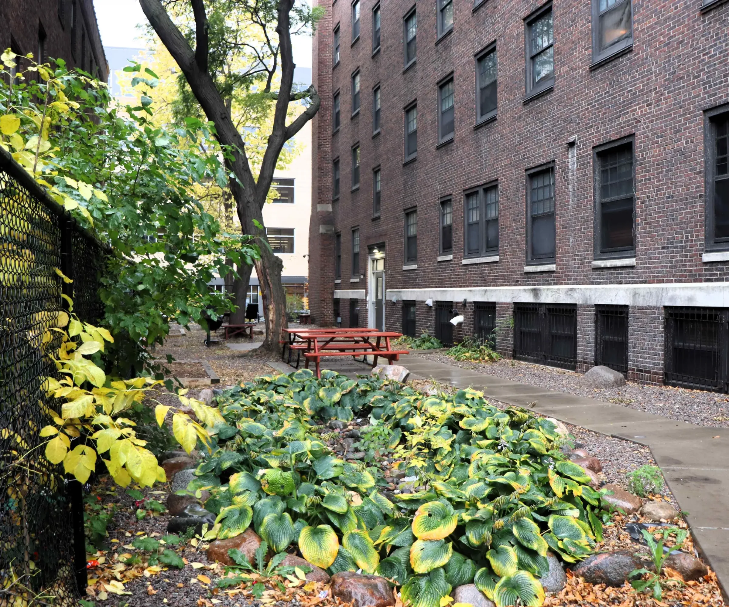 Aeon Affordable Homes and Community A serene garden courtyard with green plants and picnic tables connects the brick buildings of our affordable apartment homes.