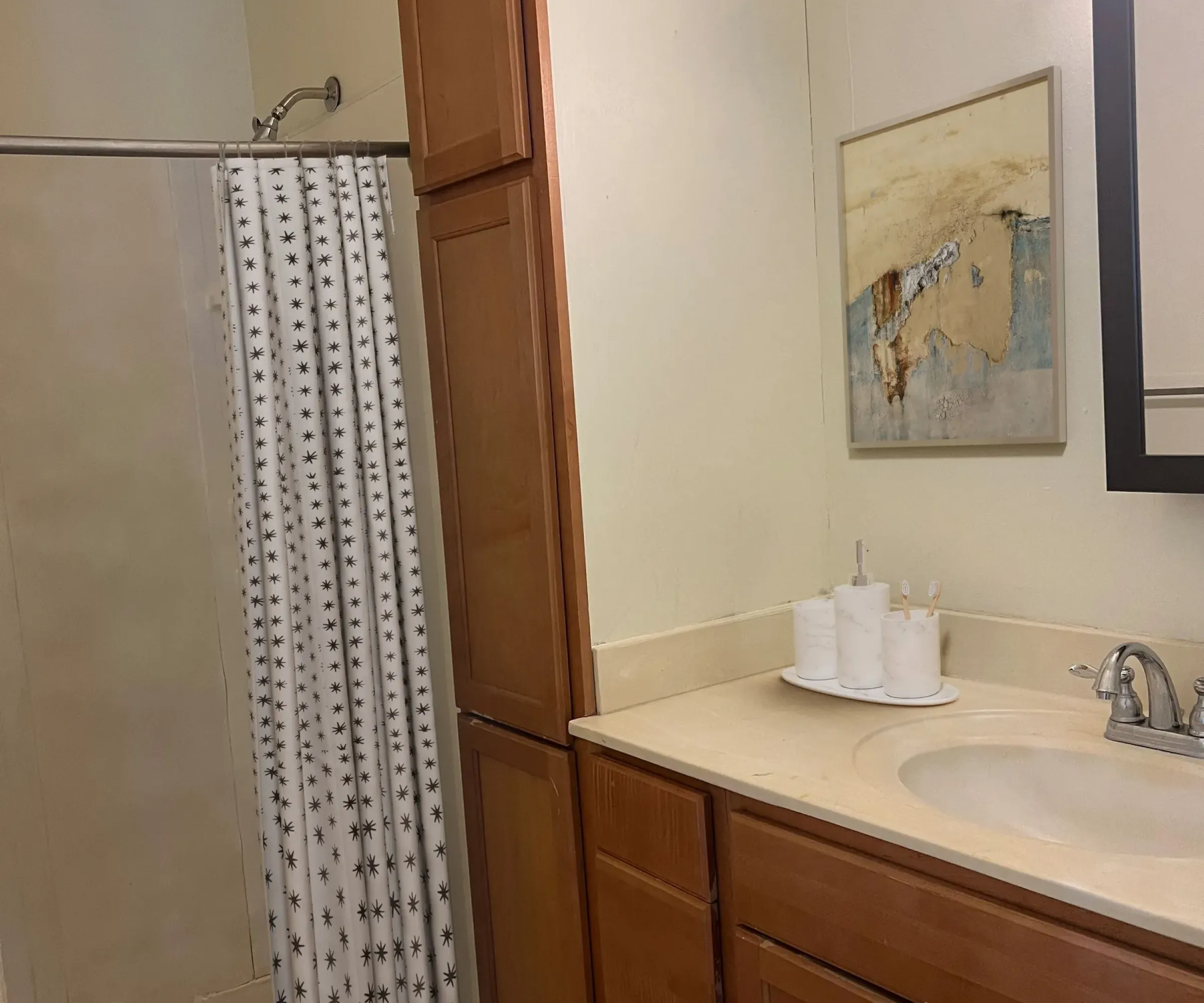 Aeon Affordable Homes and Community Affordable apartment homes featuring a bathroom with a shower, star-patterned curtain, wooden cabinets, sink, and wall art above the towel holder.
