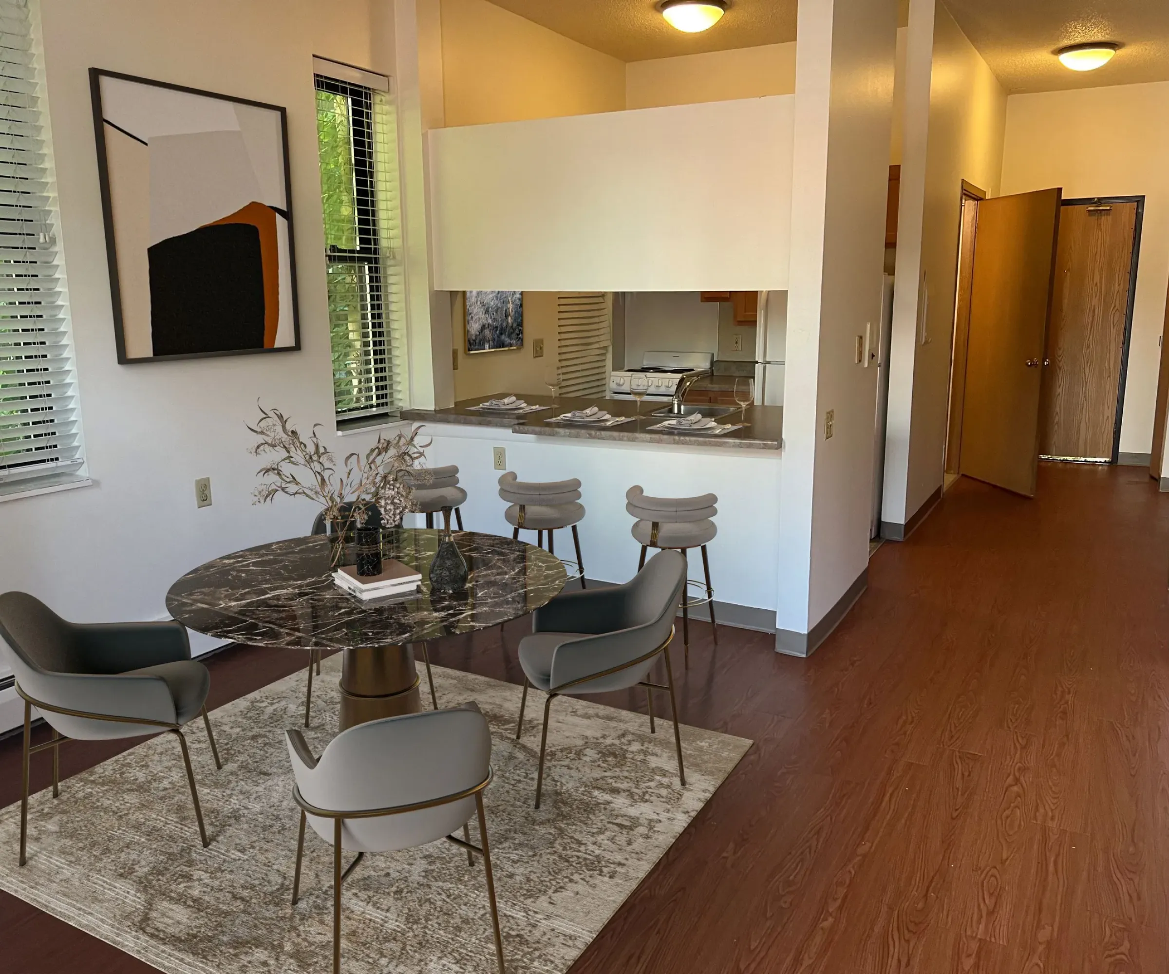 Aeon Affordable Homes and Community Modern dining room in affordable apartment homes with marble table, gray chairs, and abstract wall art, leading to kitchen and hallway.
