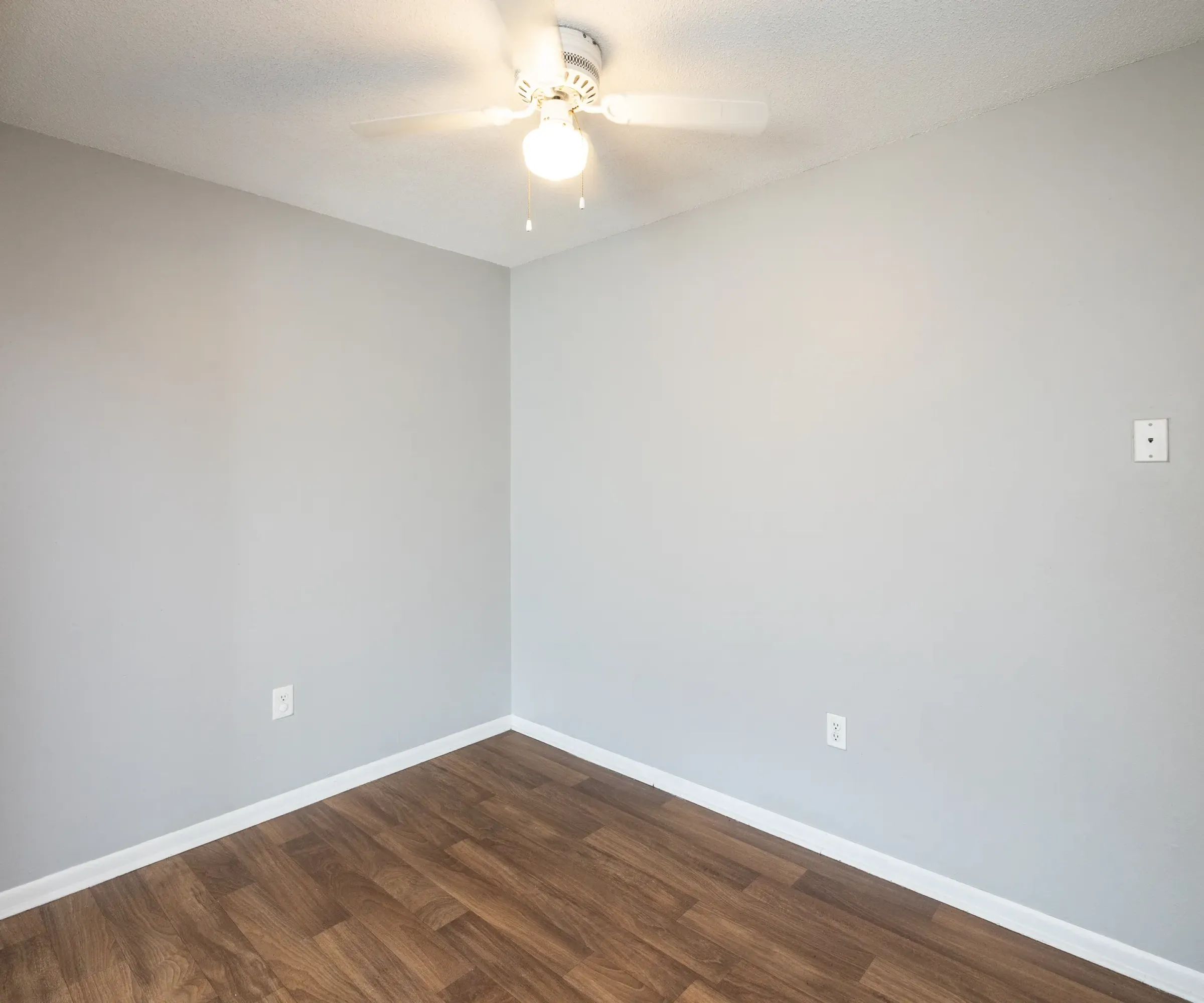 Aeon Affordable Homes The small room in Blooming Meadows South features gray walls, a wooden floor, and a white ceiling fan.