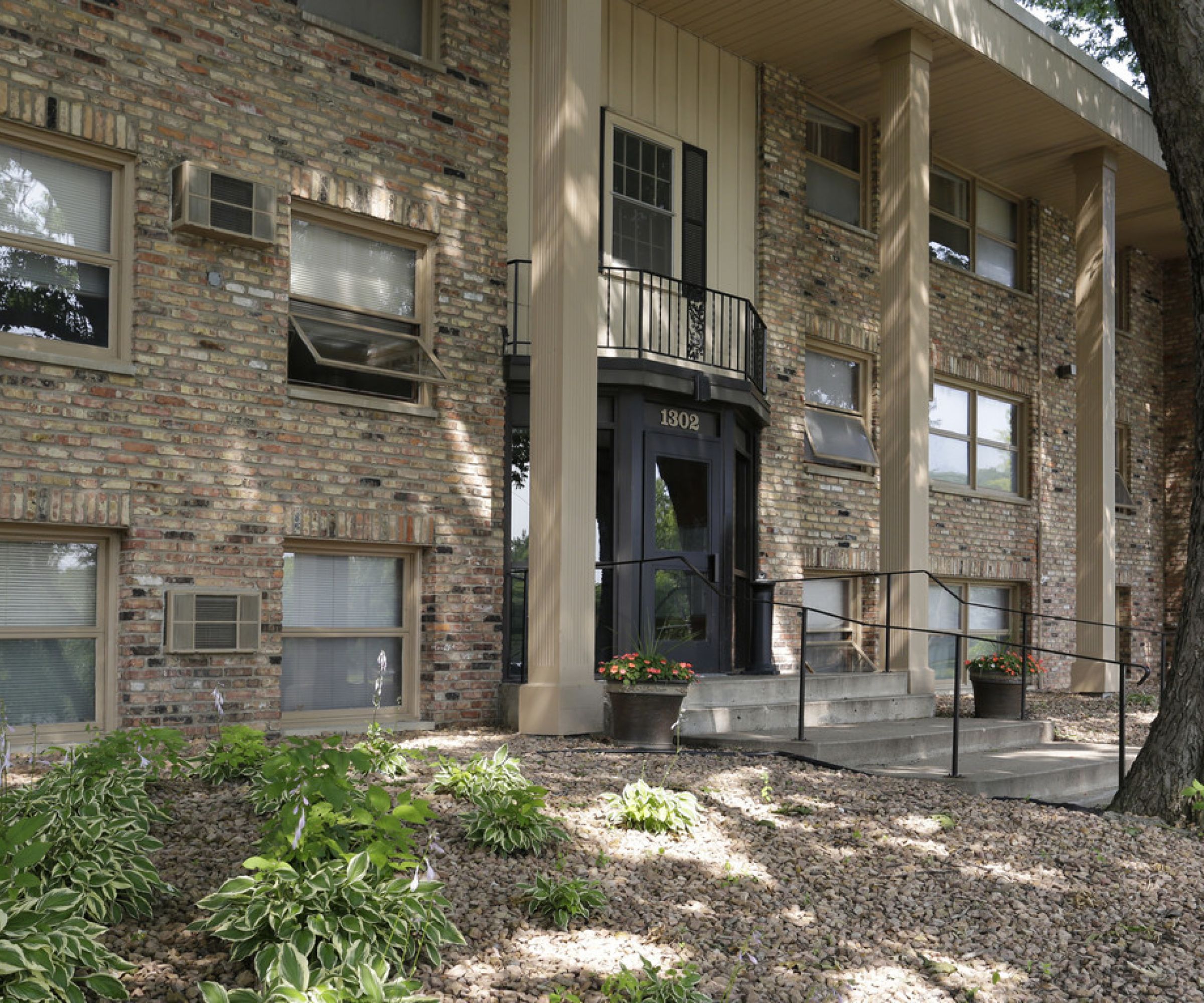 Aeon Affordable Homes and Community Affordable apartment homes in a brick building with a central entrance, surrounded by trees and landscaping, featuring steps and a ramp.
