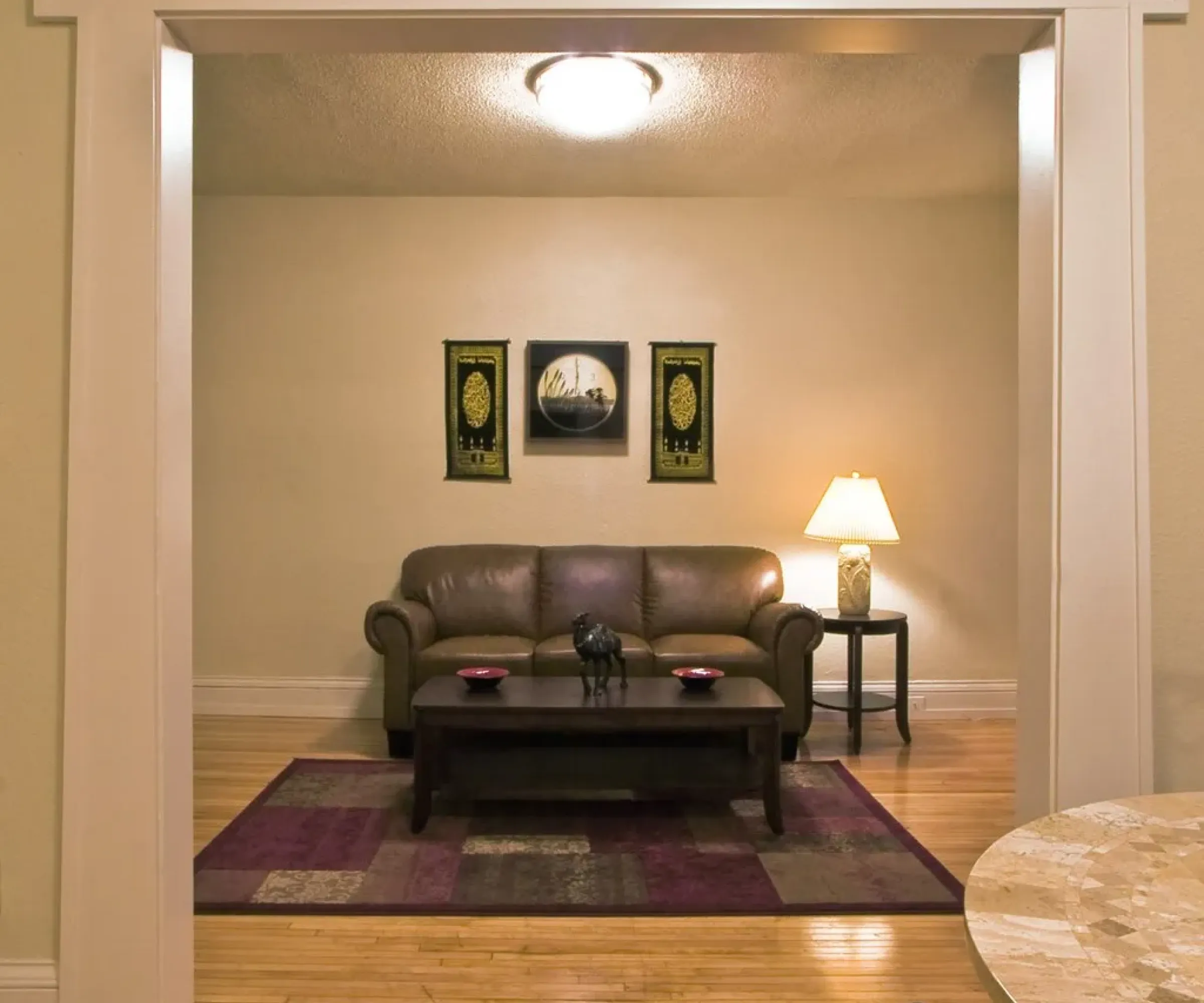 Aeon Affordable Homes Cozy living room with a brown sofa, coffee table, table lamp, and decorative wall art on wooden flooring.
