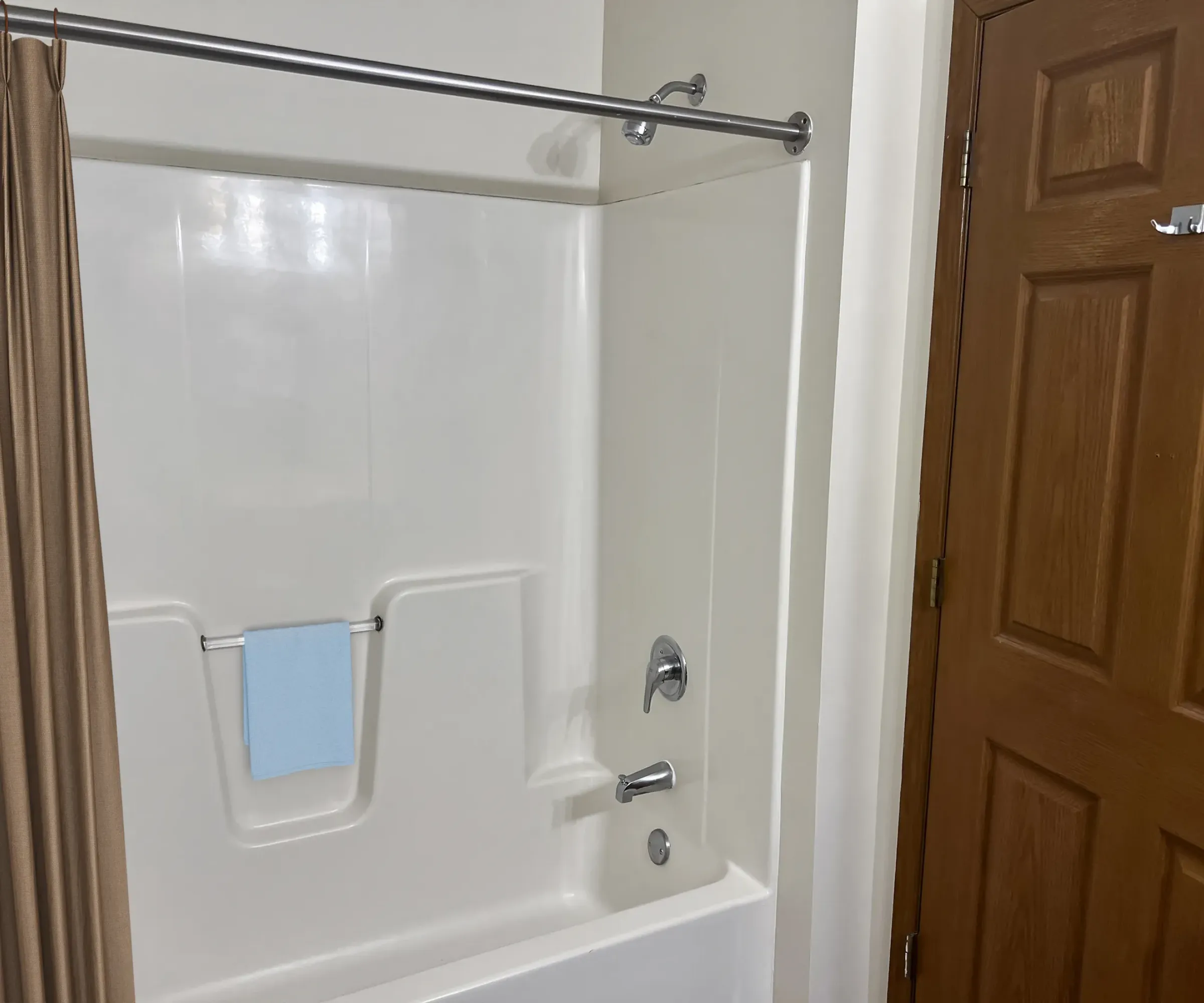 Aeon Affordable Homes and Community Affordable apartment homes with a bathroom featuring a white bathtub, brown curtain, blue towel on the rack, and a wooden door.