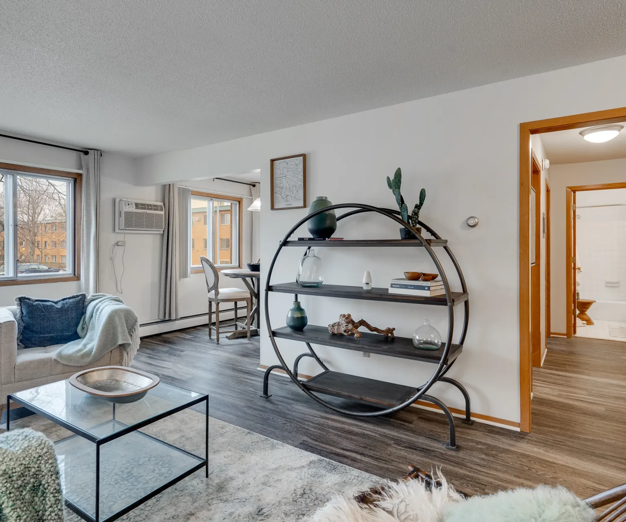 Aeon Affordable Homes Modern living room with a circular shelf, plants, glass coffee table, and large window. Bathroom visible in hallway.