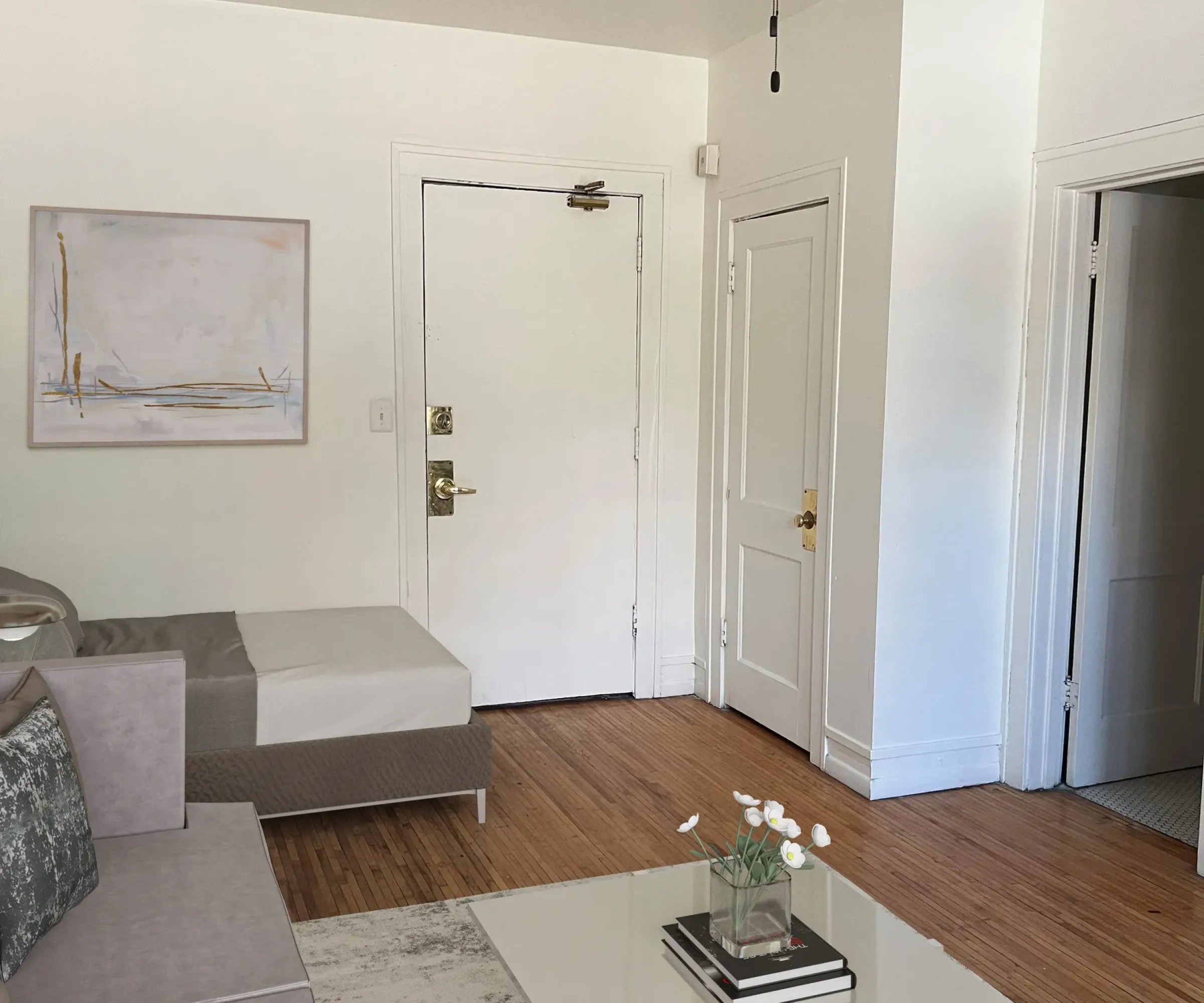 Aeon Affordable Homes and Community Minimalist and affordable apartment homes feature a gray sectional sofa, glass coffee table, ceiling fan, and light wood flooring.