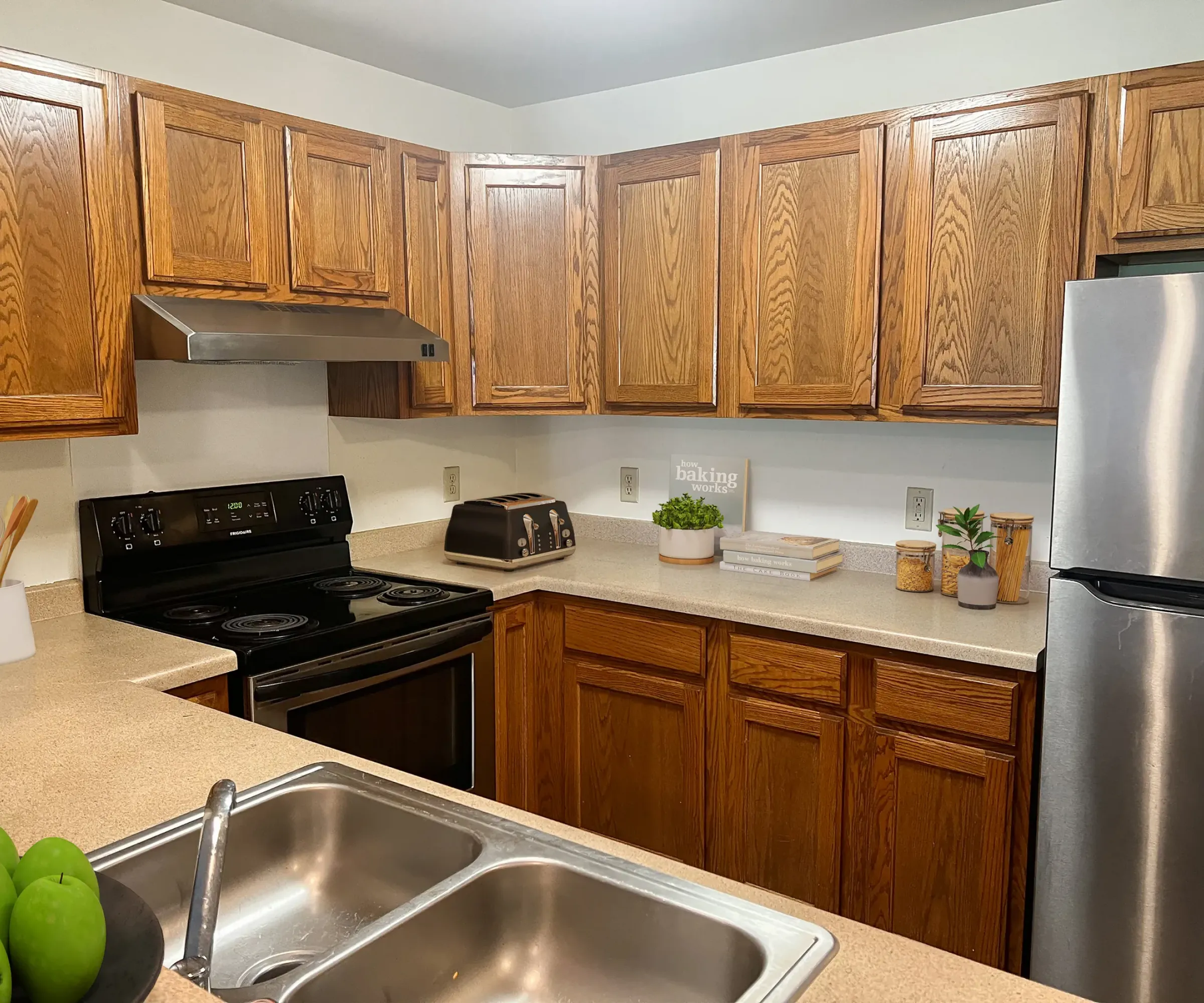 Aeon Affordable Homes and Community Affordable apartment homes featuring a kitchen with wooden cabinets, stainless steel appliances, double sink, and stylish countertop decor.