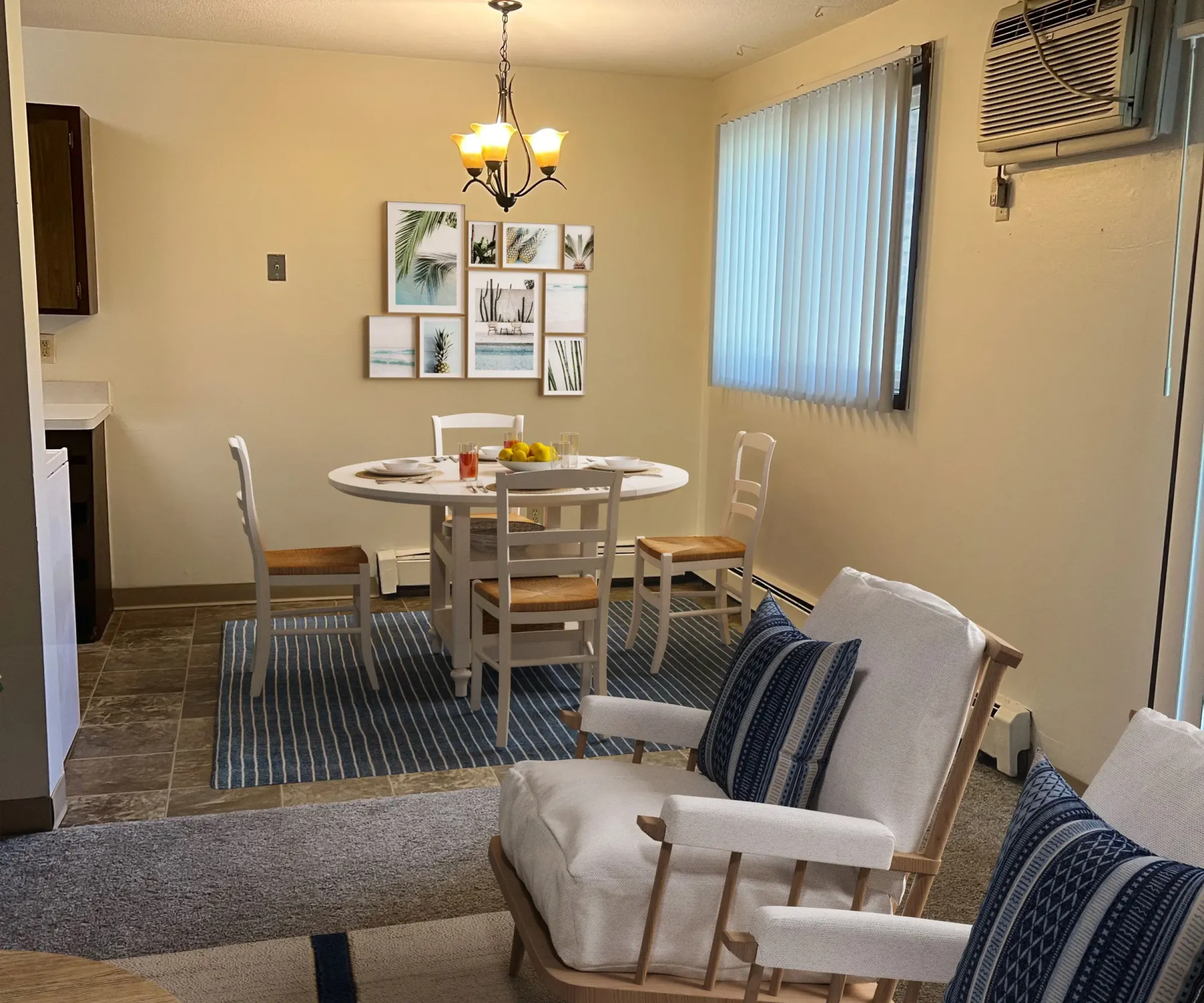 Aeon Affordable Homes and Community Cozy dining and living area in affordable apartment homes with a round table, chairs, armchairs, wall art, and an air conditioner.