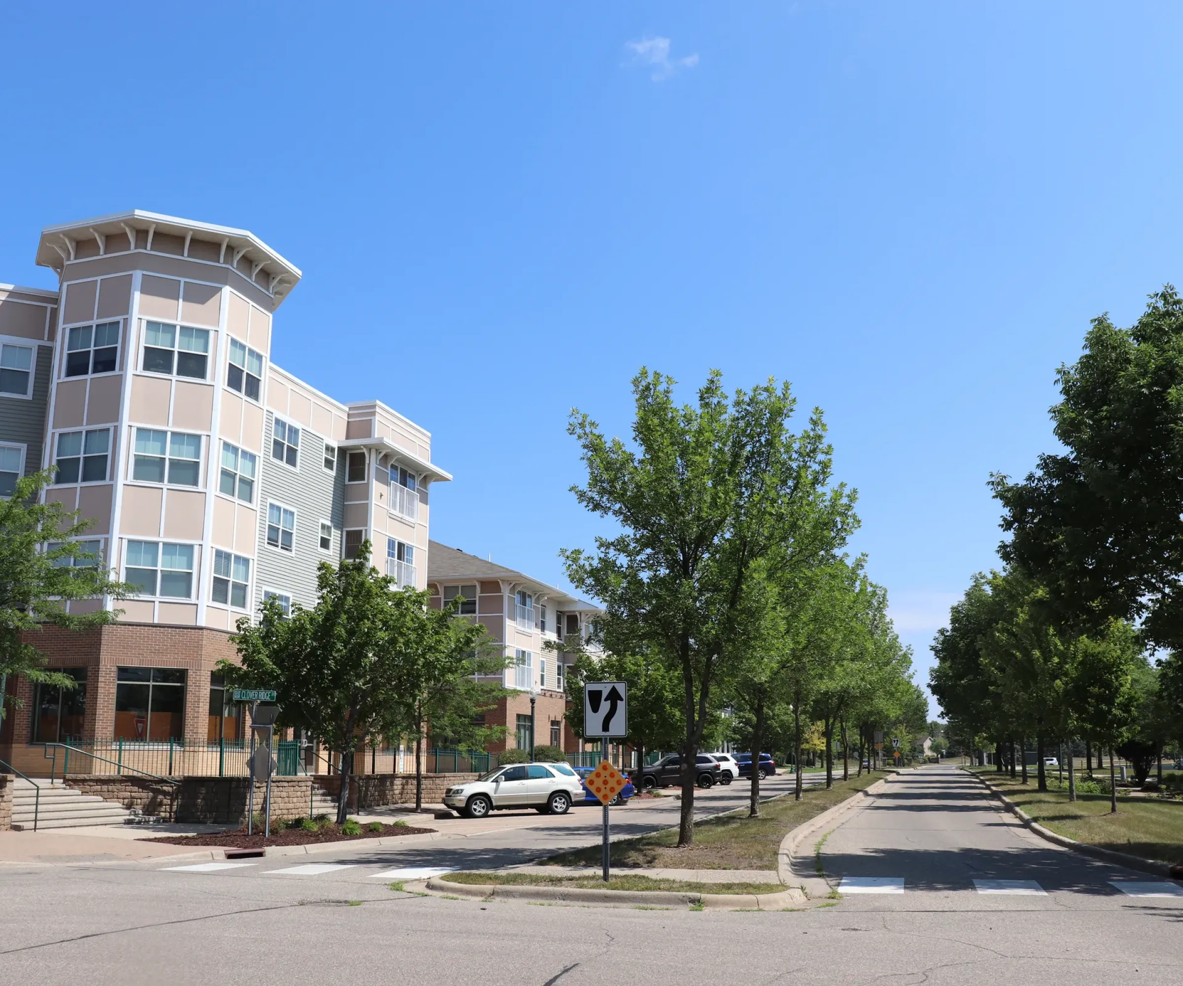 Aeon Affordable Homes and Community Street view of modern, four-story affordable apartment homes with trees lining the road and cars parked along the sidewalk.