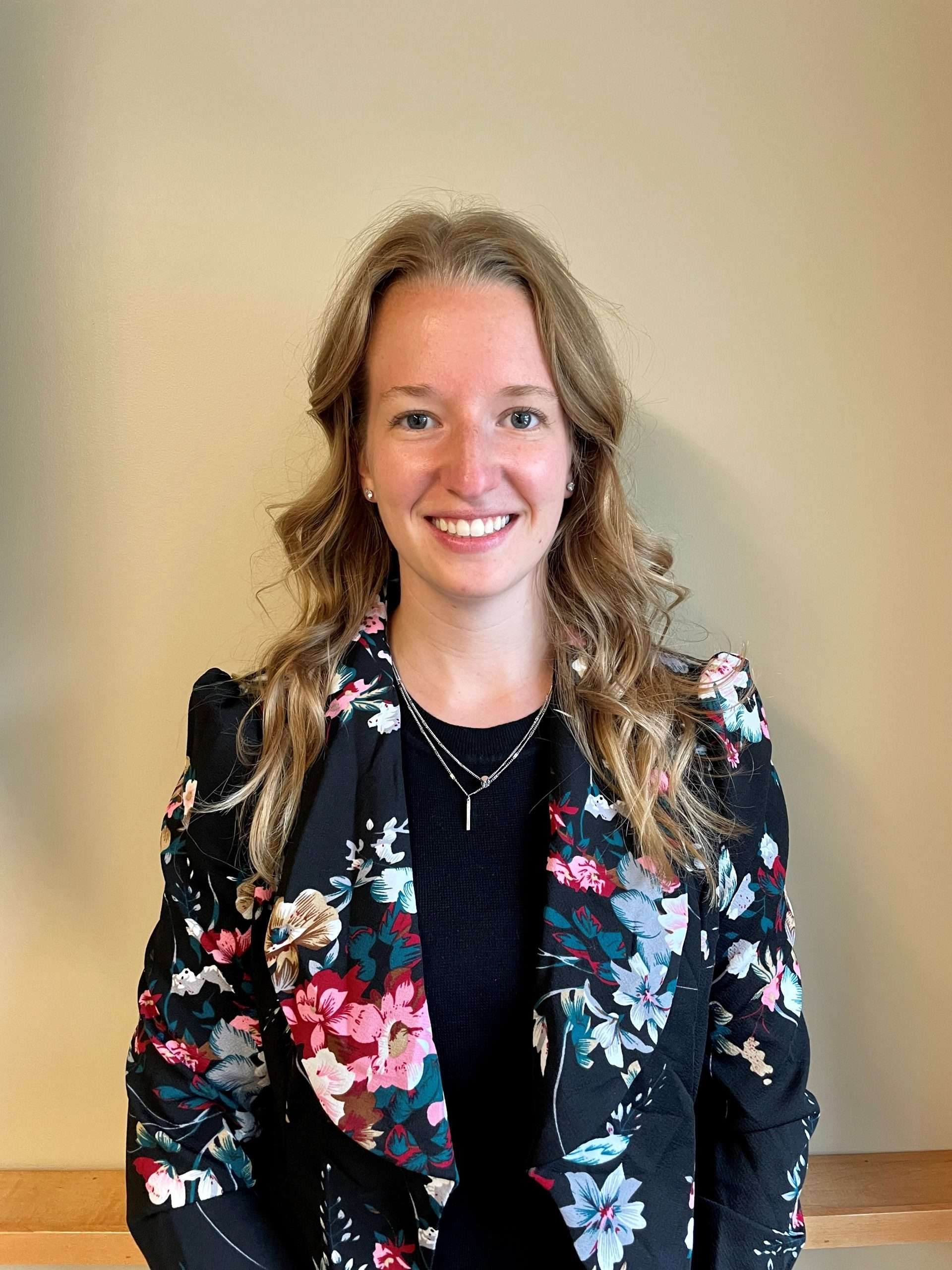 Aeon Affordable Homes and Community Person smiling, wearing a floral-patterned blazer over a black top, standing against a plain beige background. Aeon Affordable Homes and Community Person in a floral blazer and black top smiling against a beige background. Nicole Icenogle headshot Nicole Icenogle headshot