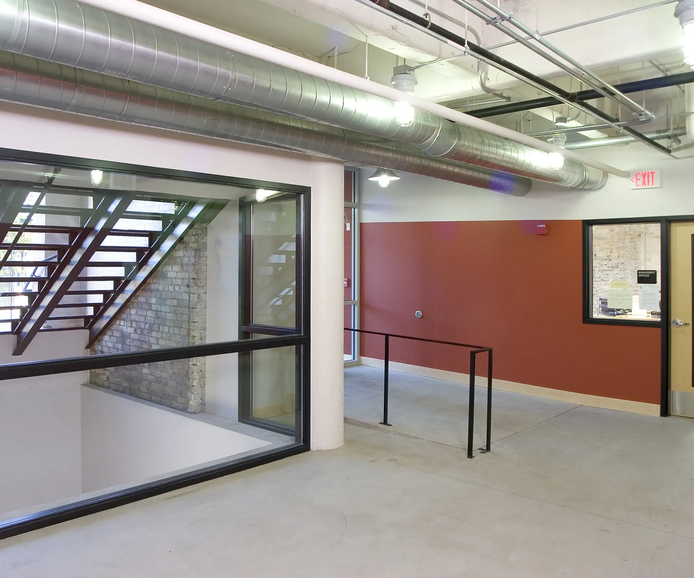 Aeon Affordable Homes and Community Affordable apartment homes featuring an industrial-style interior with exposed ducts, a staircase, large windows, and a red accent wall.
