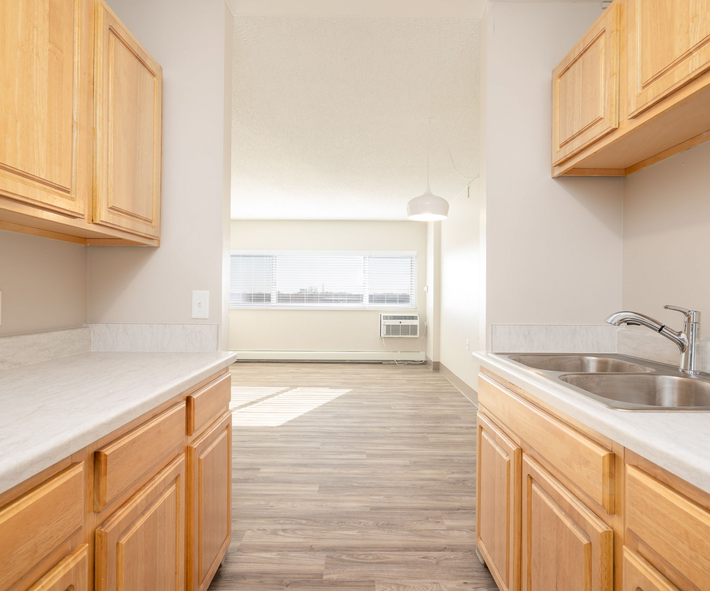 Aeon Affordable Homes and Community Bright kitchen with light wood cabinets, gray countertops, and a view into a sunlit room in our affordable apartment homes.
